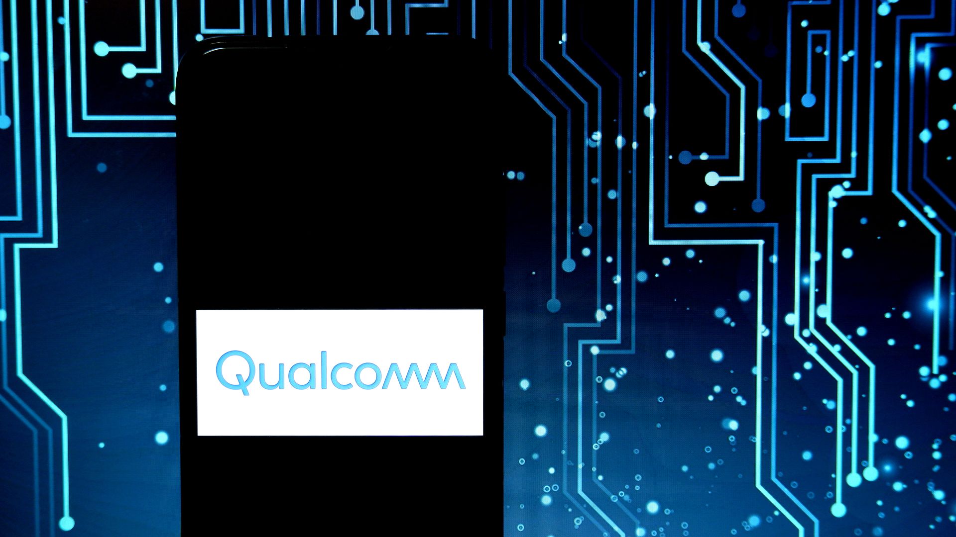 A photo illustration of the Qualcomm logo displayed on a smartphone with a graphic depicting a circuitboard behind it.