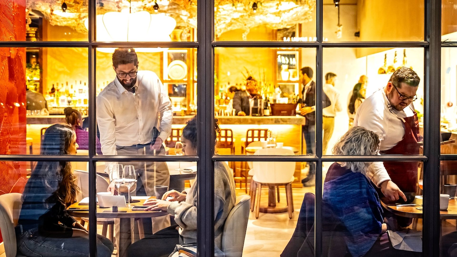 A restaurant from the outside window view with two tables being helped by serving staff