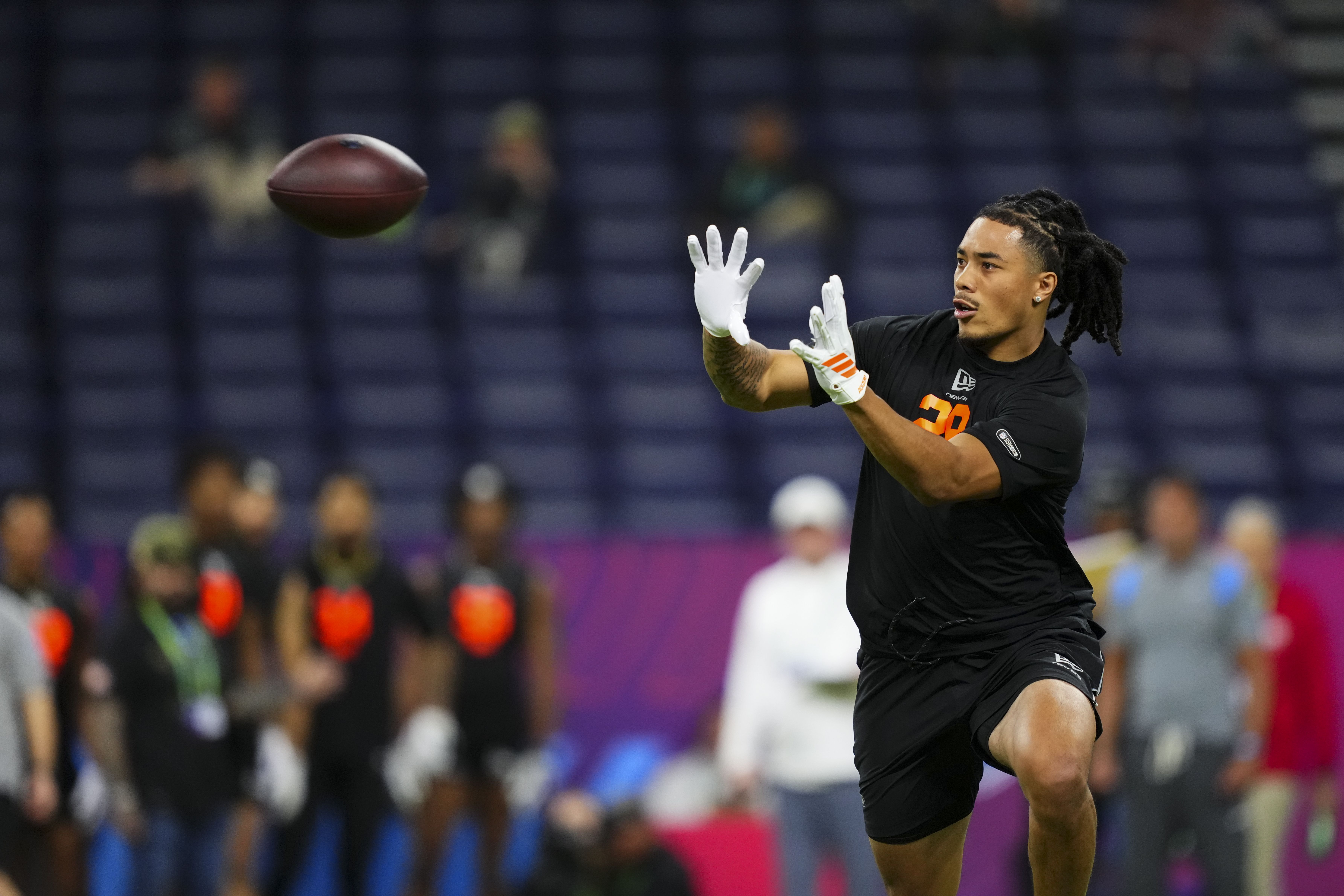 A young man wearing black workout clothes holds out his white gloved hands to catch an arriving football.