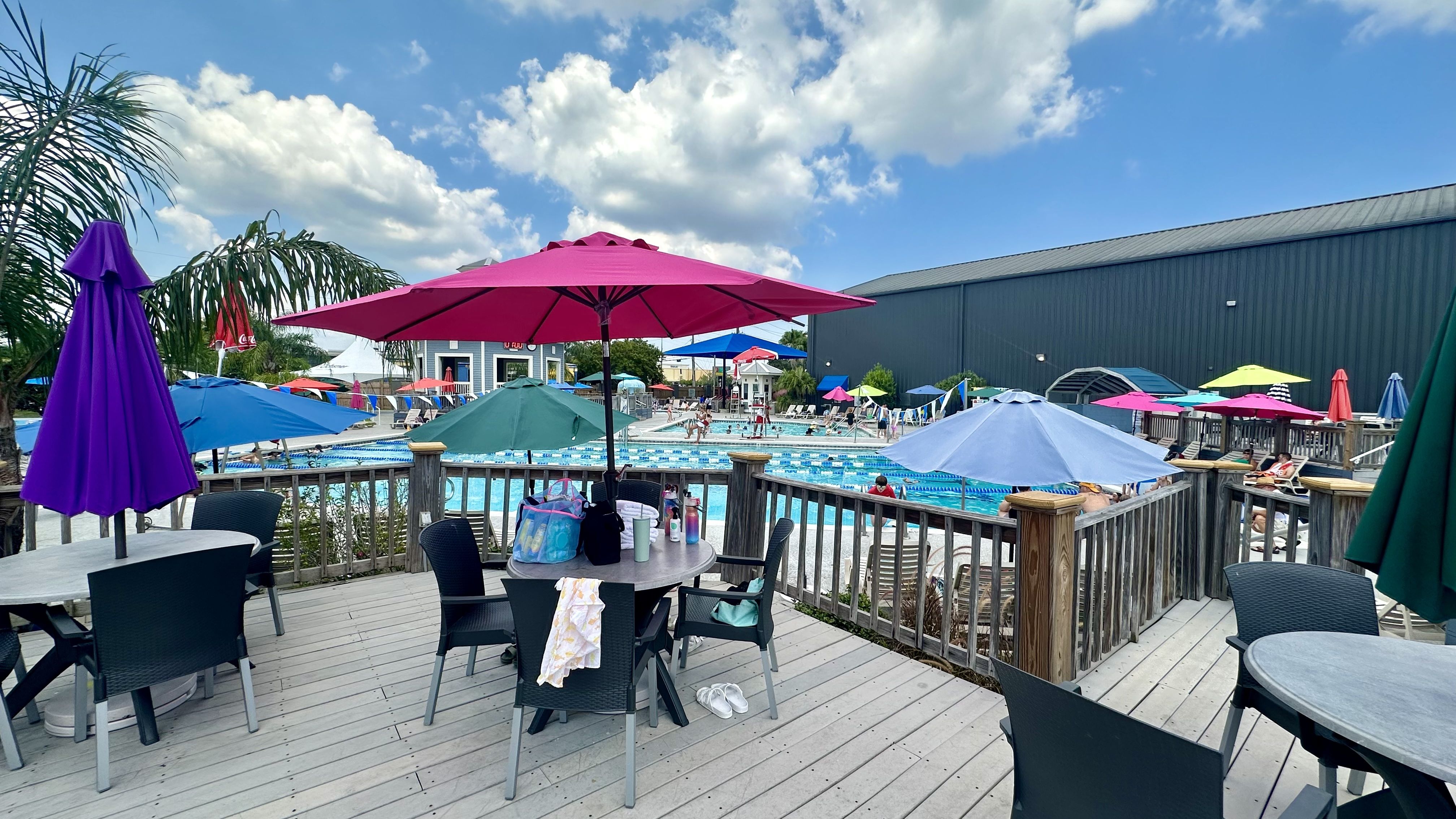 Photo shows a table and umbrellas by a pool