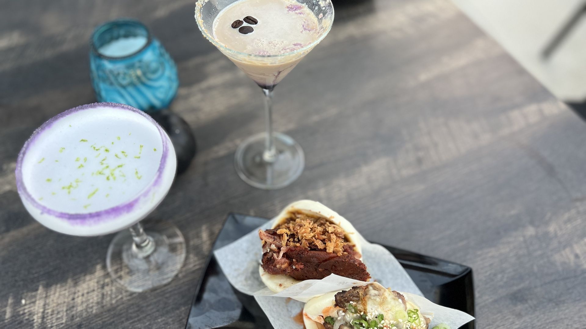 A light-filled table with two cocktails and two buns.