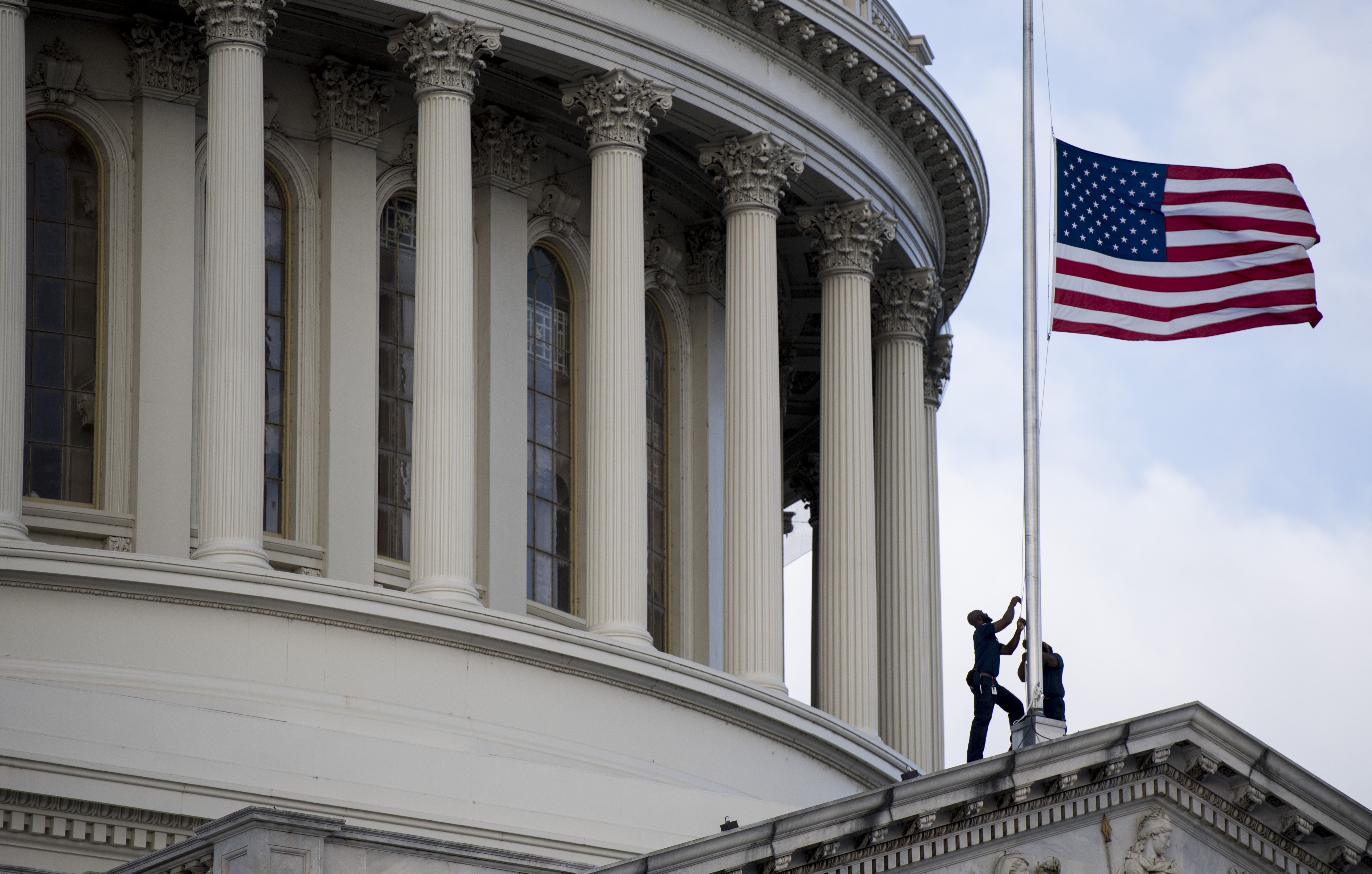 Capitol workers lower the flag to half staff after the passing of Cummings.