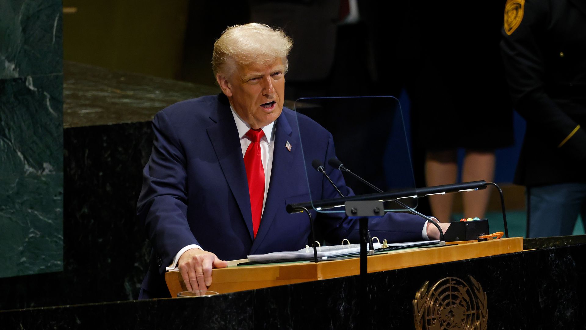 President Trump, wearing a navy jacket, white shirt and red tie, speaks at a podium.