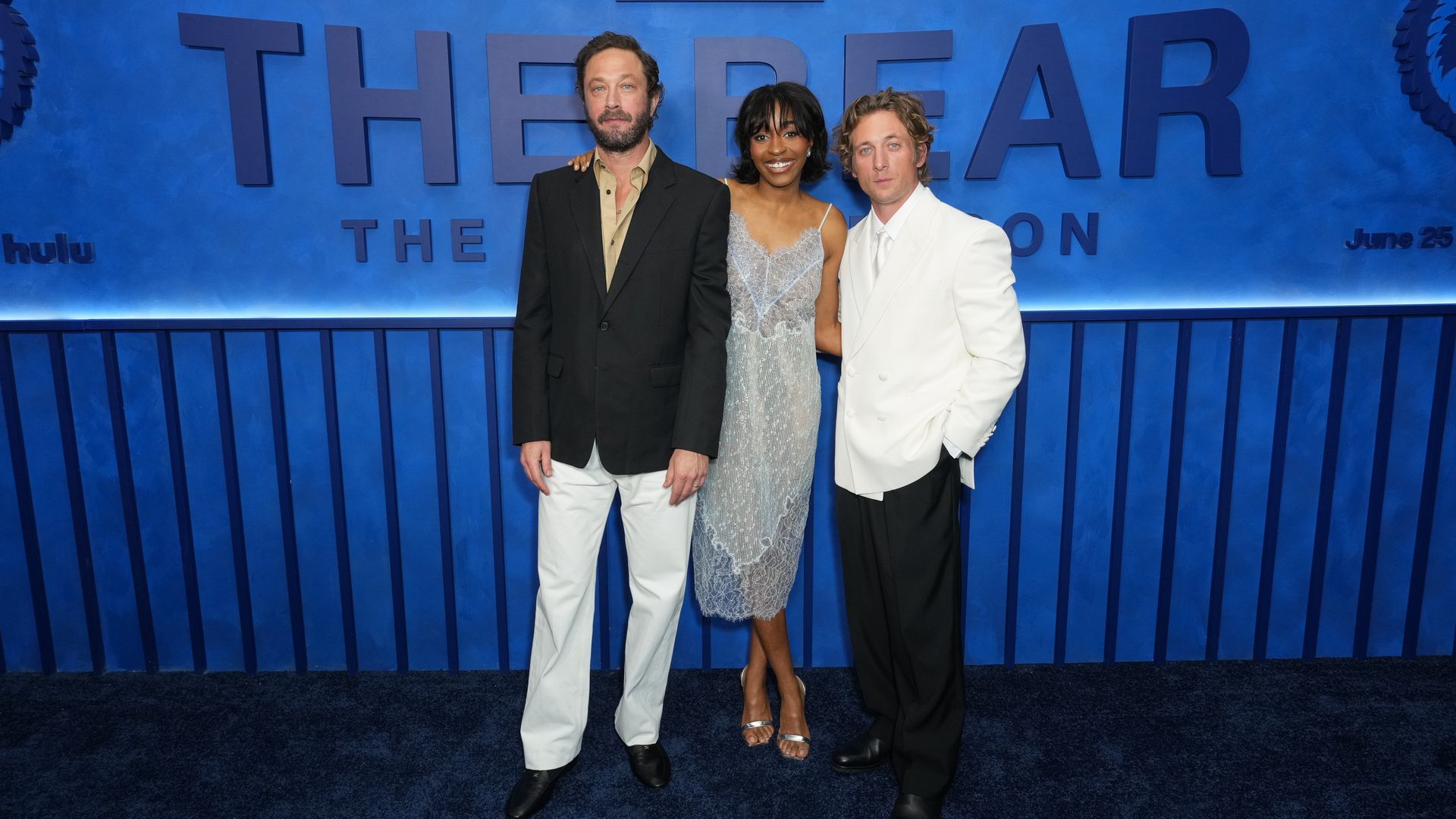 Actors Ebon Moss-Bachrach, Ayo Edebiri and Jeremy Allen White stand in front of a "THE BEAR" sign.