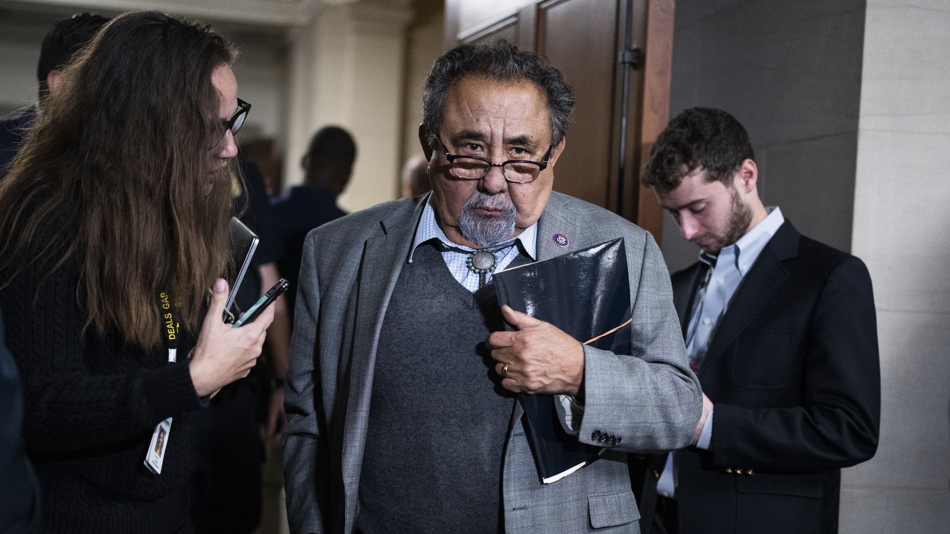 Rep. Raul Grijalva, wearing a light gray suit and walking through a hallway while surrounded by press.