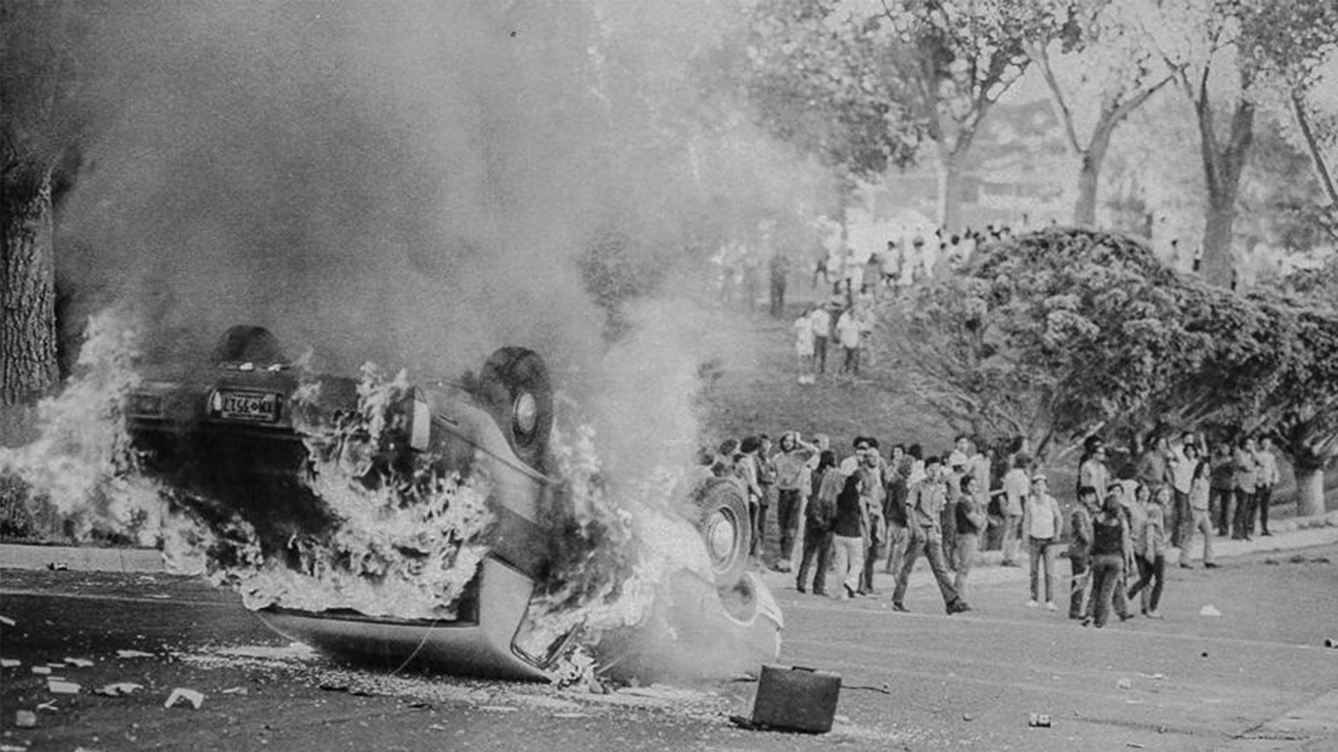 An overturned car burns as Mexican American demonstrators watch during a 1971 protest in Albuquerque.