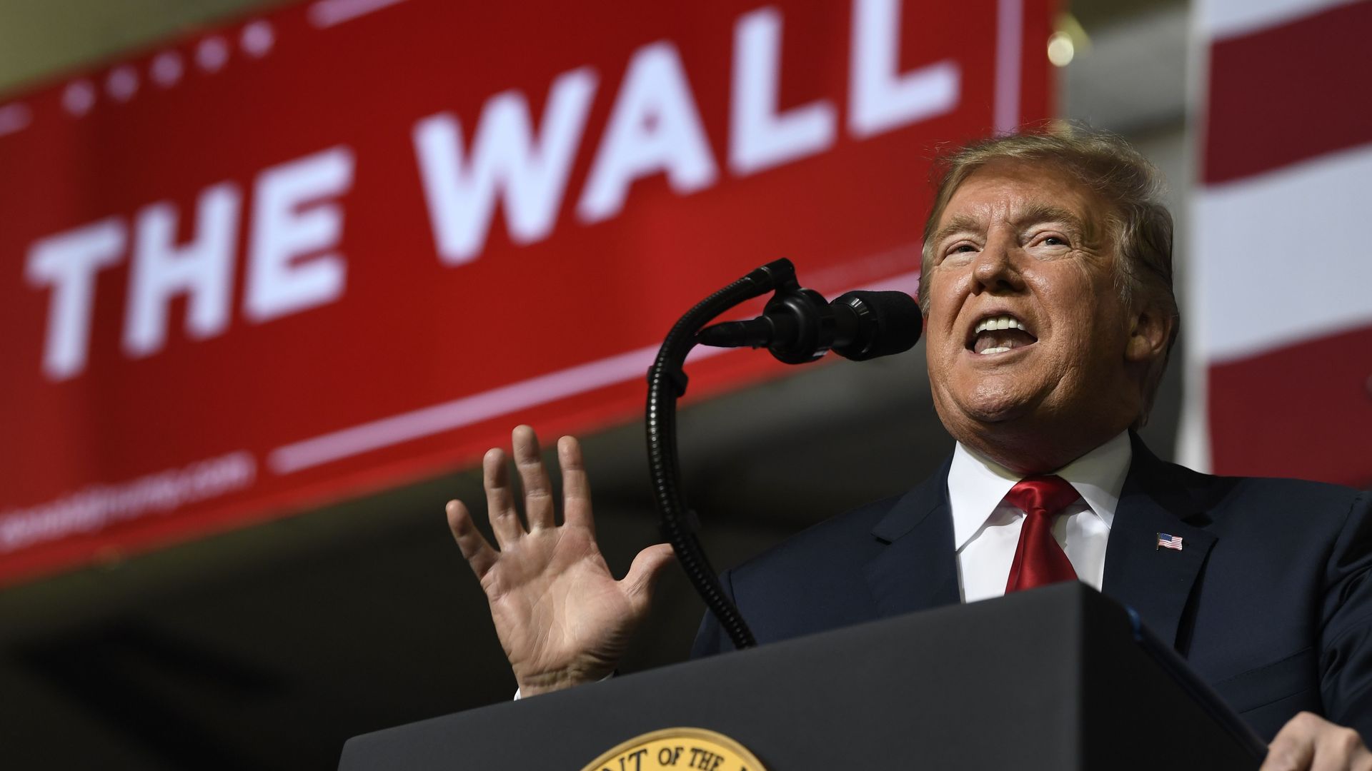 Donald Trump giving a speech, with "Build the Wall" in the background