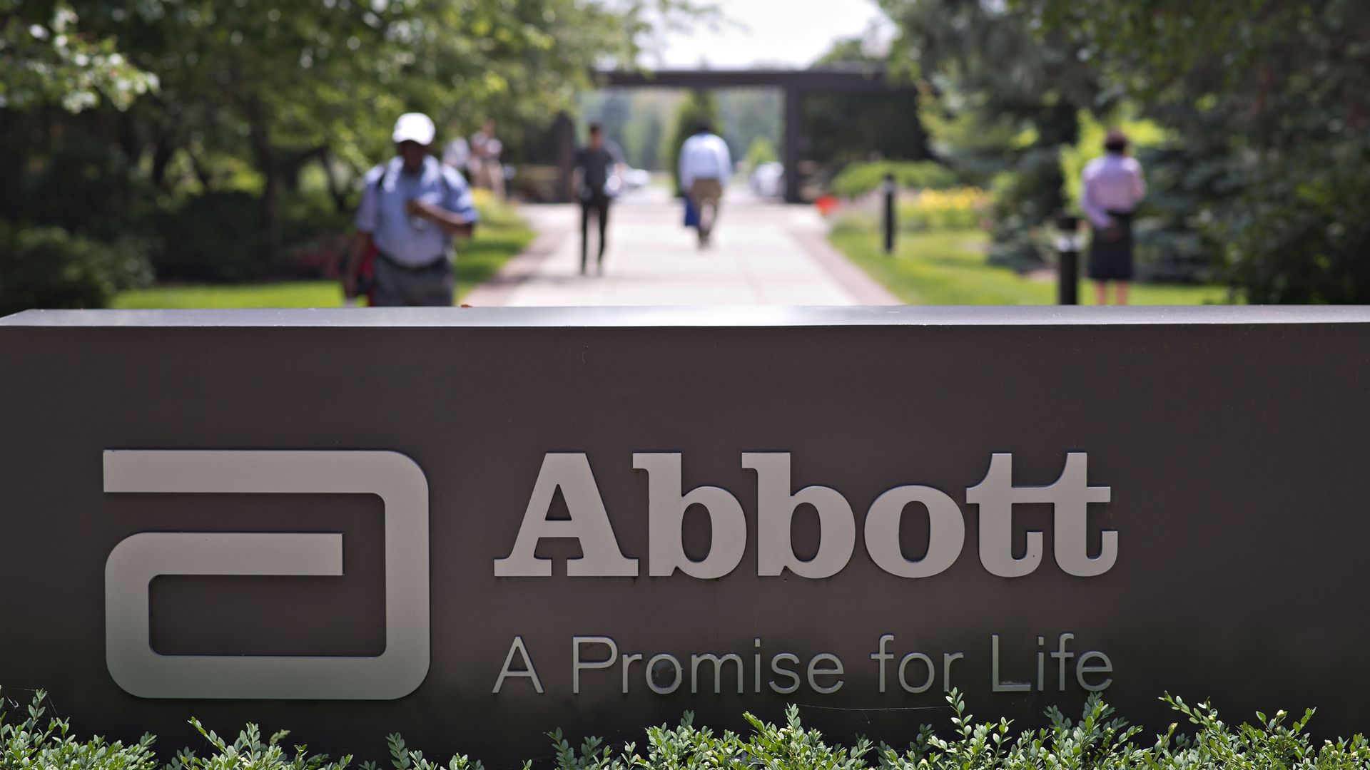 Employees walk near an Abbott Laboratories sign at the company's headquarters complex in Abbott Park, Illinois.
