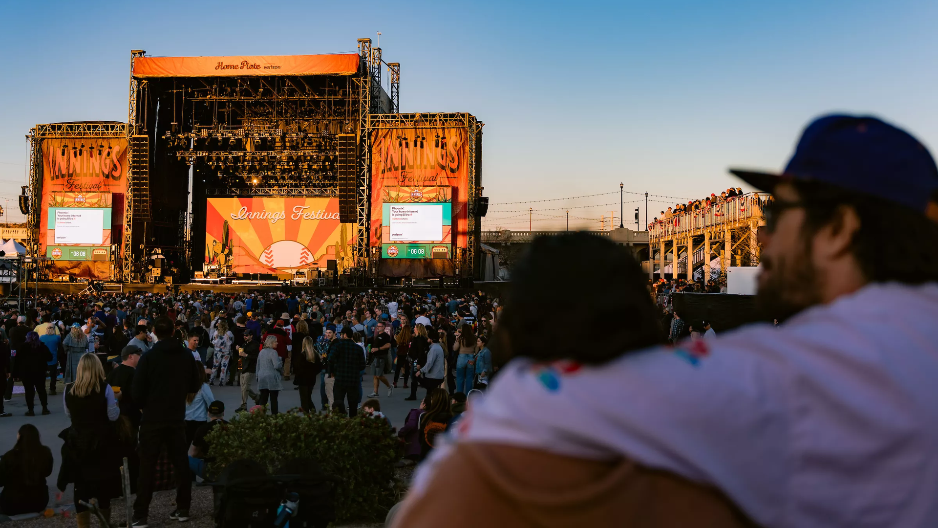 A music festival crowd in front of a stage at sundown