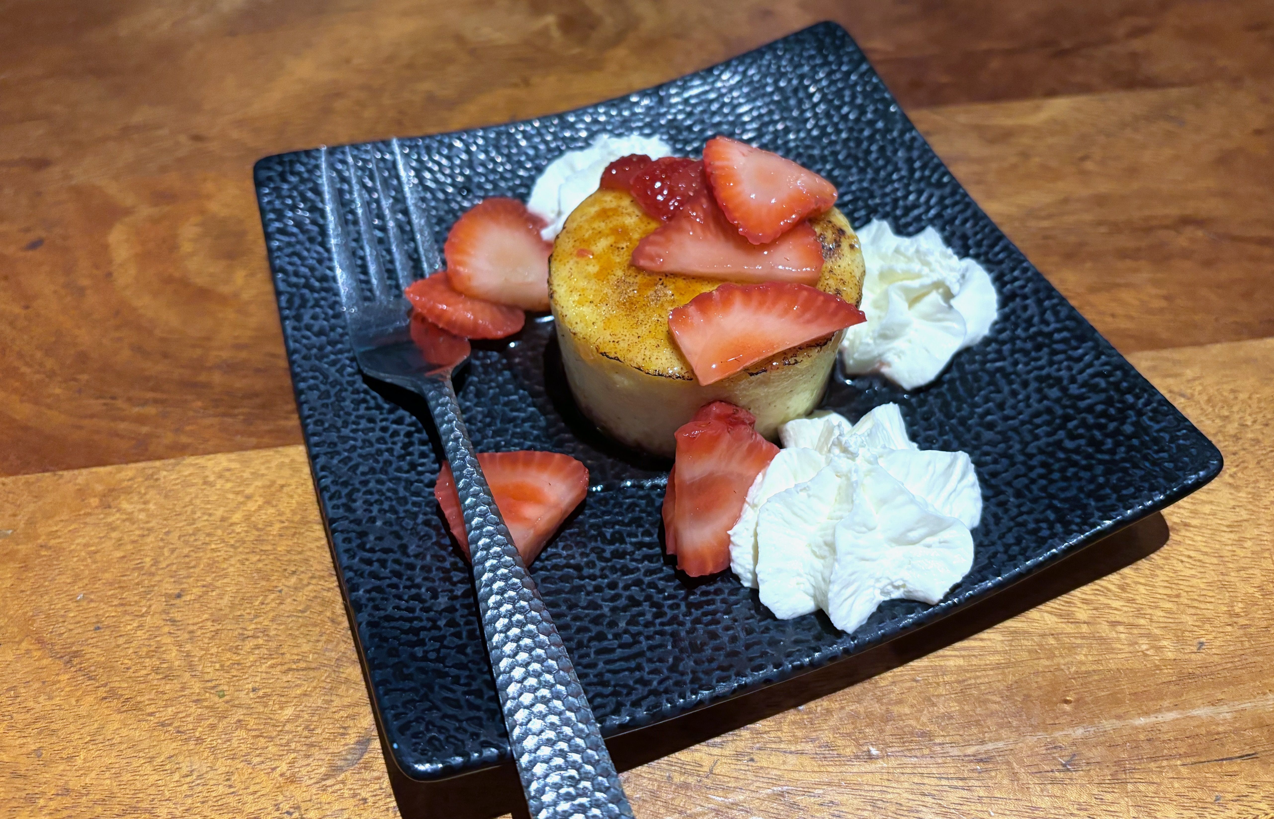 A bruleed cheesecake topped with cut strawberries and three dabs of whipped cream