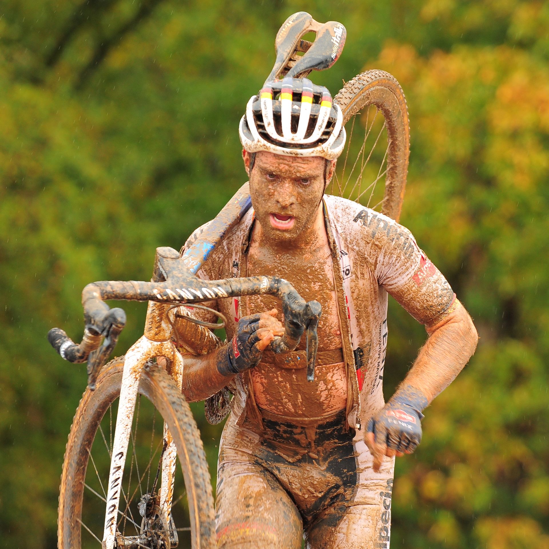 A muddy cyclist climbs to the top of a stone feature before riding down the other side. 