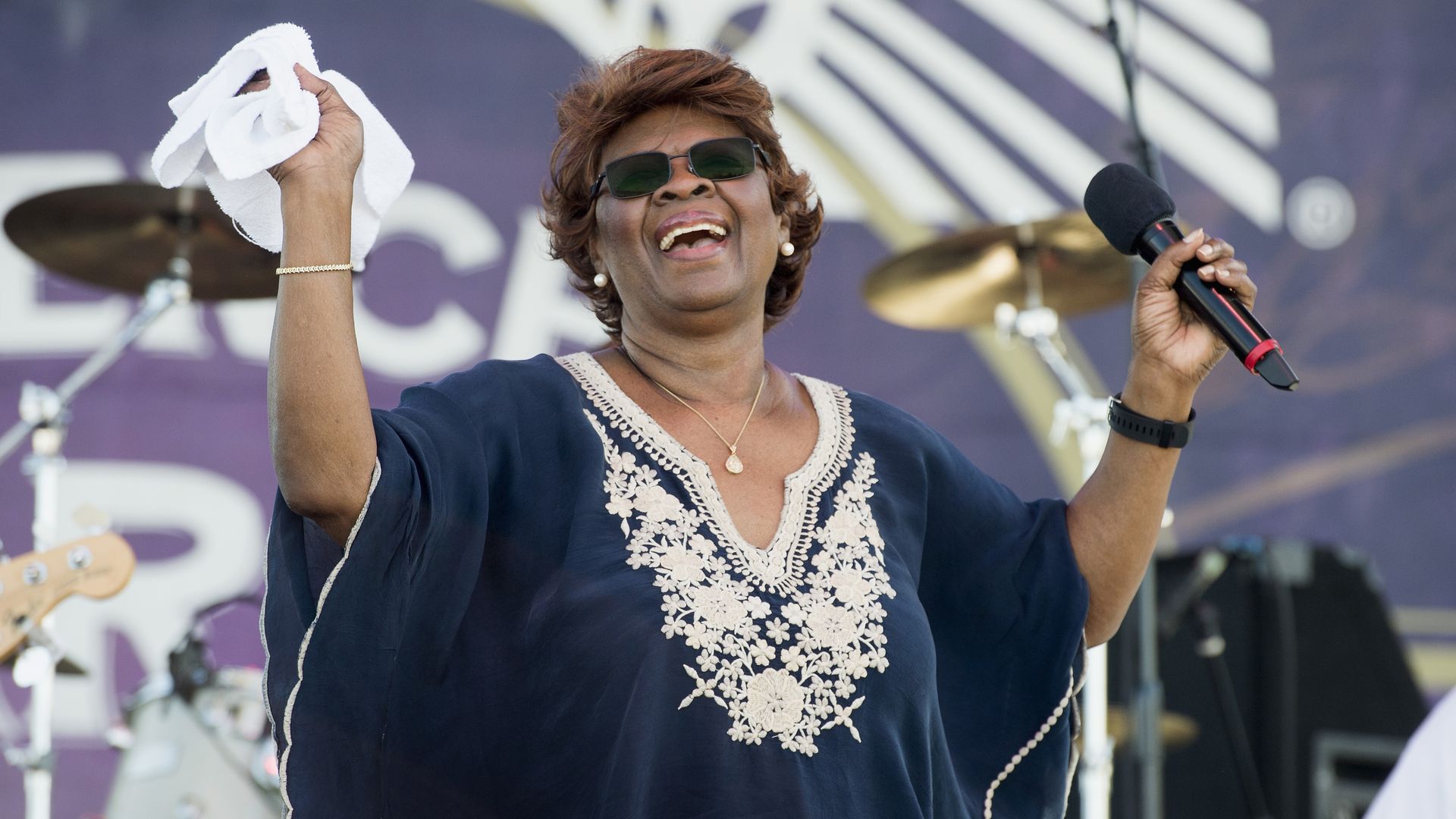 A woman holds up a white kerchief in one hand and a microphone in the other onstage.