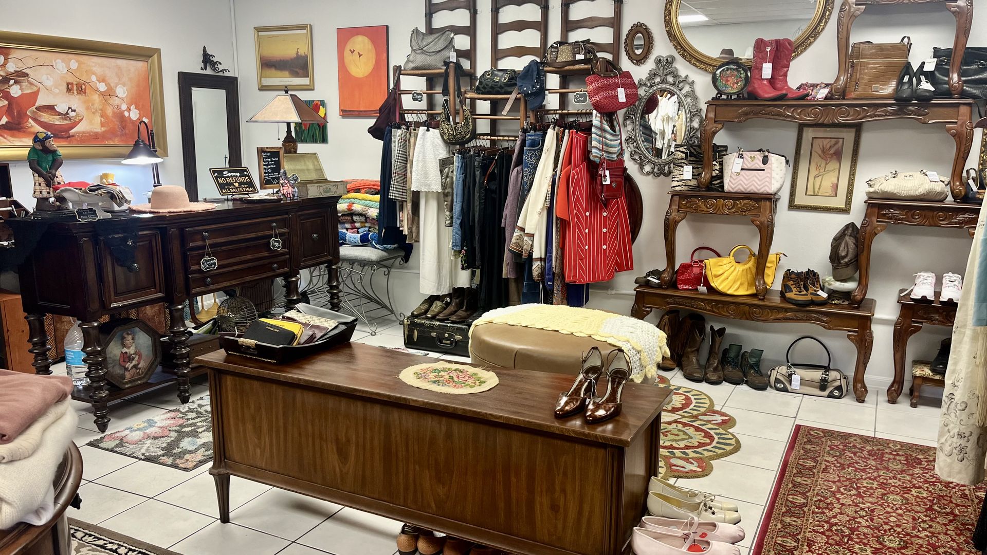 A shop with racks of colorful vintage clothing, shoes and bags decorated with mid-century modern furniture and paintings.