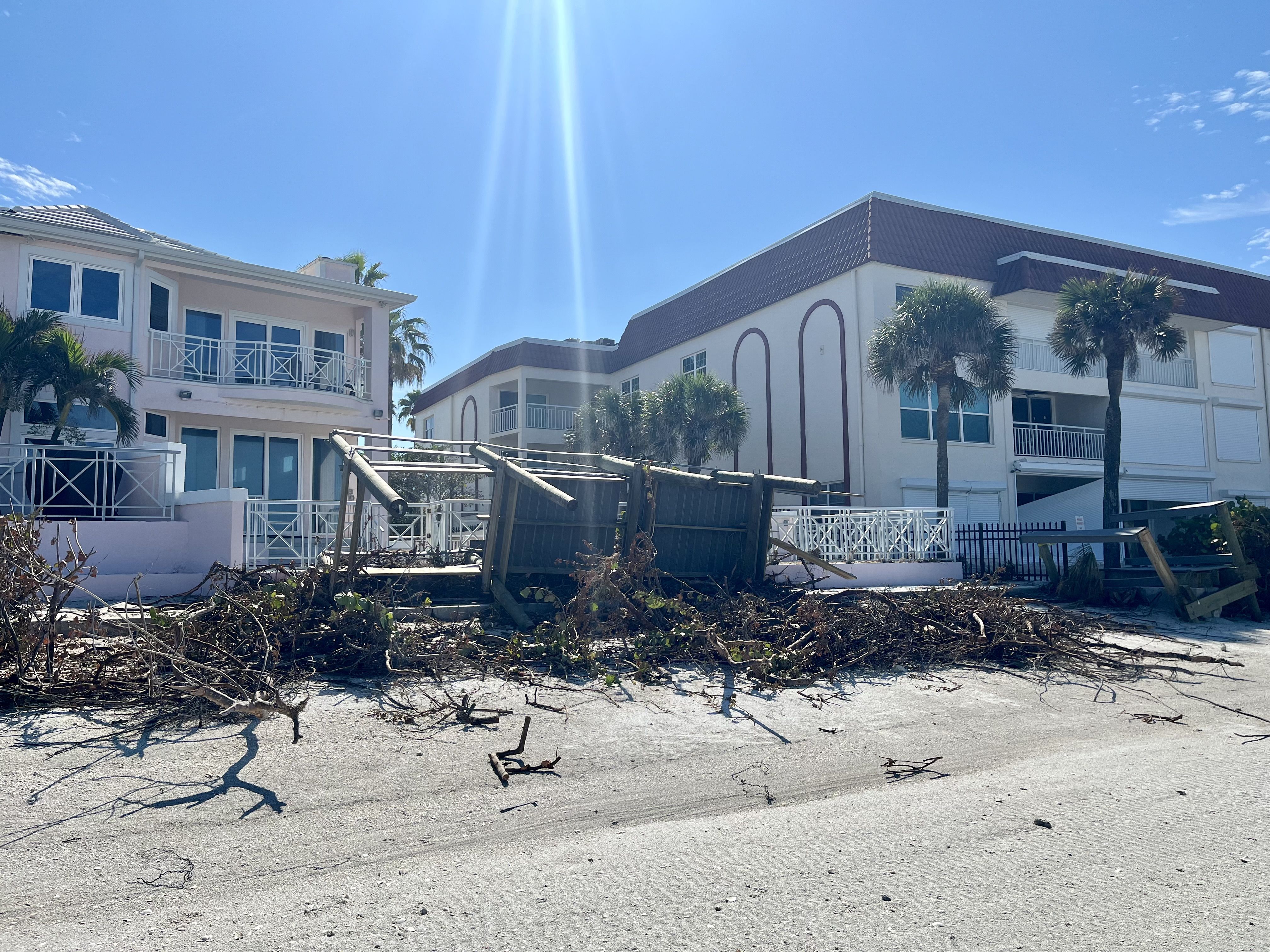 A boardwalk on the beach is pushed up against the fence of a pink house. 