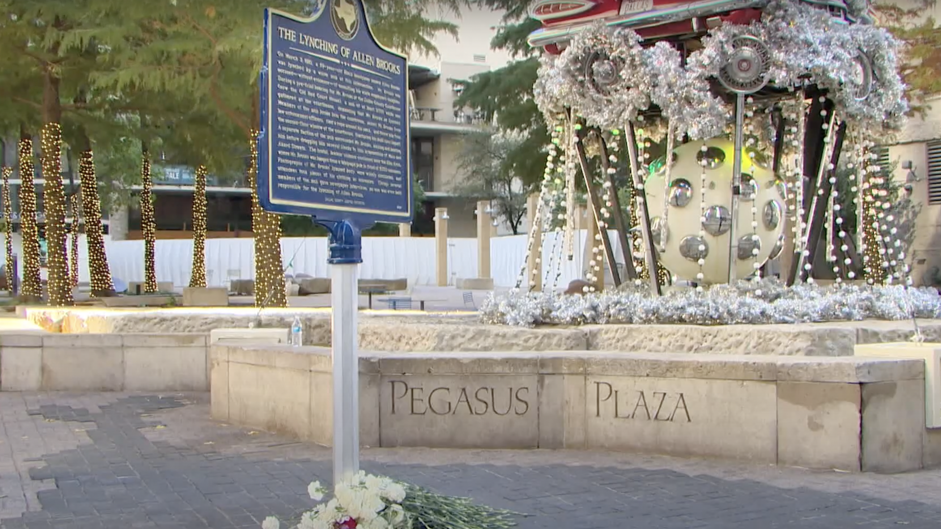 A dark brown sign with a paragraph of text on it stands in front of a concrete slab that says "Pegasus Plaza"