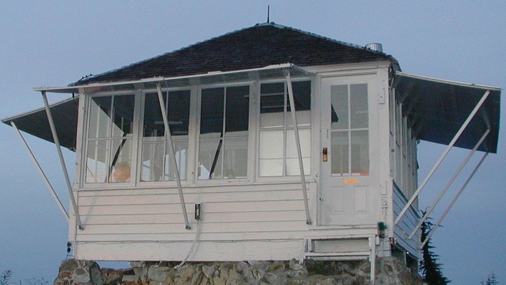 A white wooden cabin built on a bluff is among the fire lookouts people can camp in. 