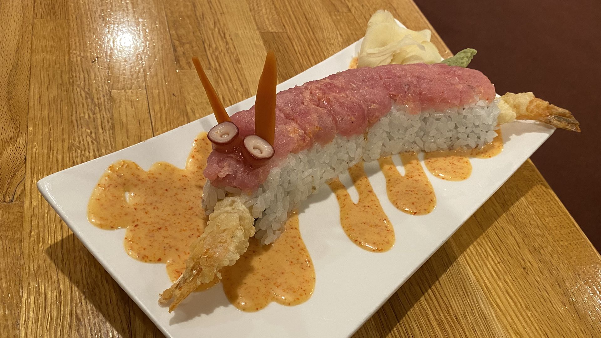 A sushi roll shaped like a dragon, with raw tuna on top and a shrimp tail in the mouth