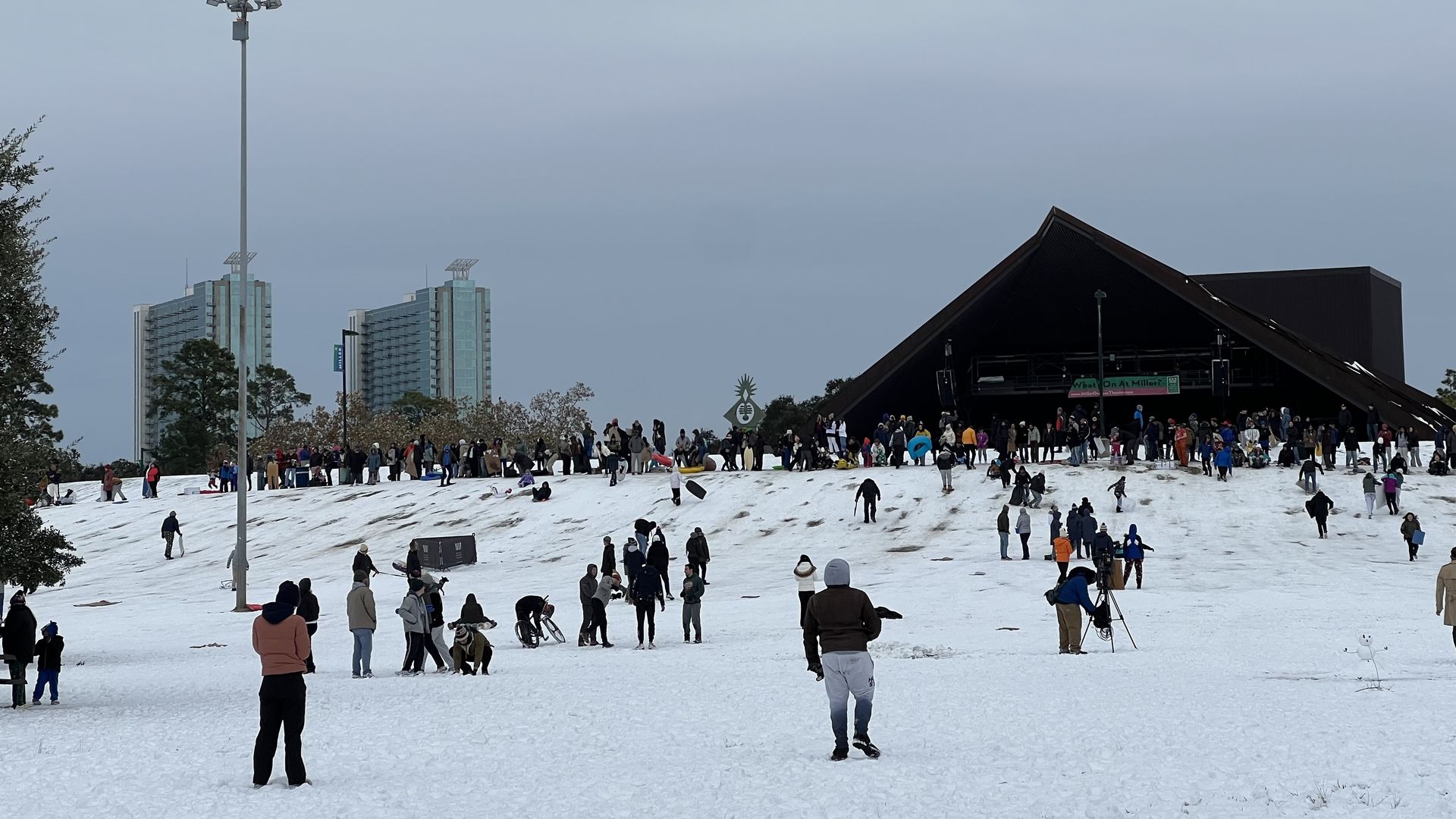 Photo of dozens of people in the snow on a hill, in front of a theater. 