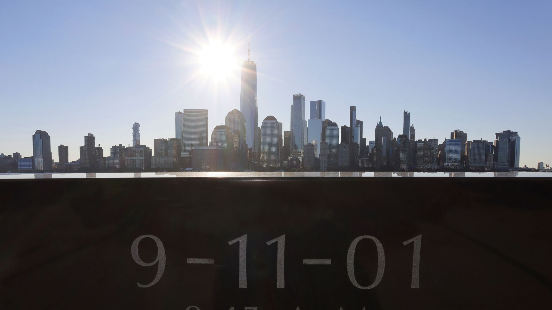 Photo of the sun rising over the Manhattan skyline with a 9-11-01 memorial in the foreground