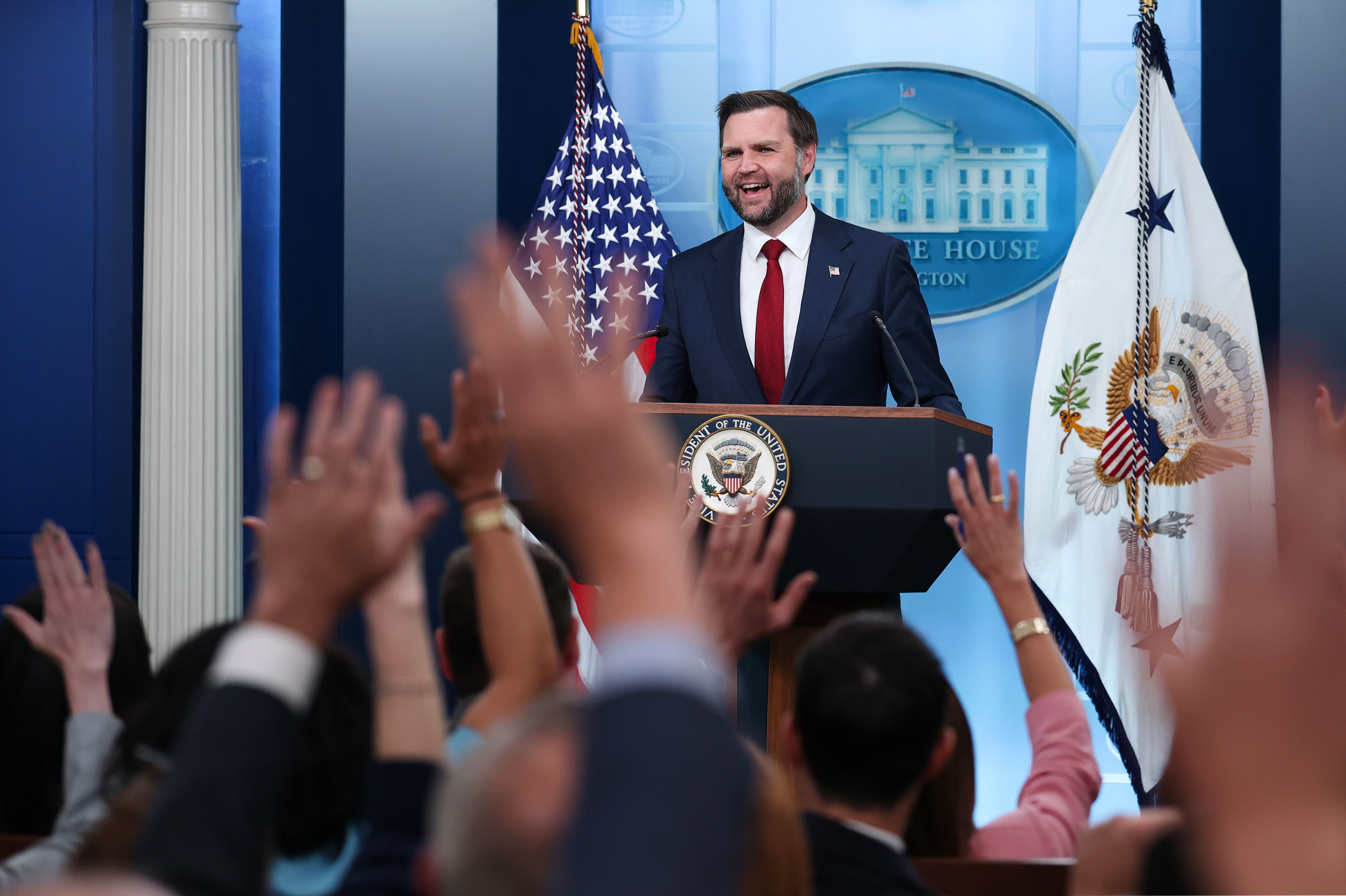 Vice President JD Vance stands behind a podium in the White House briefing room while reporters raise their hands.