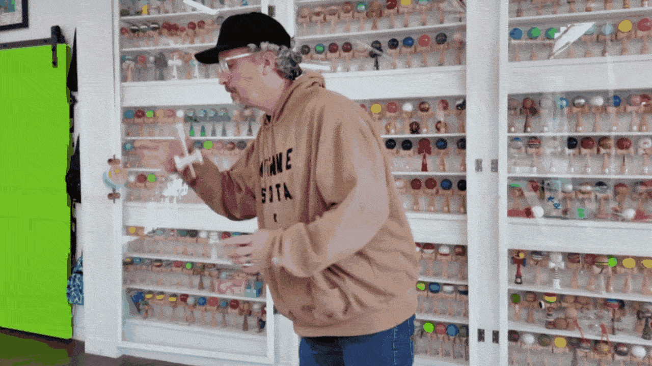 A man in a brown hoodie spins a kendama, a wooden toy with a ball and string.