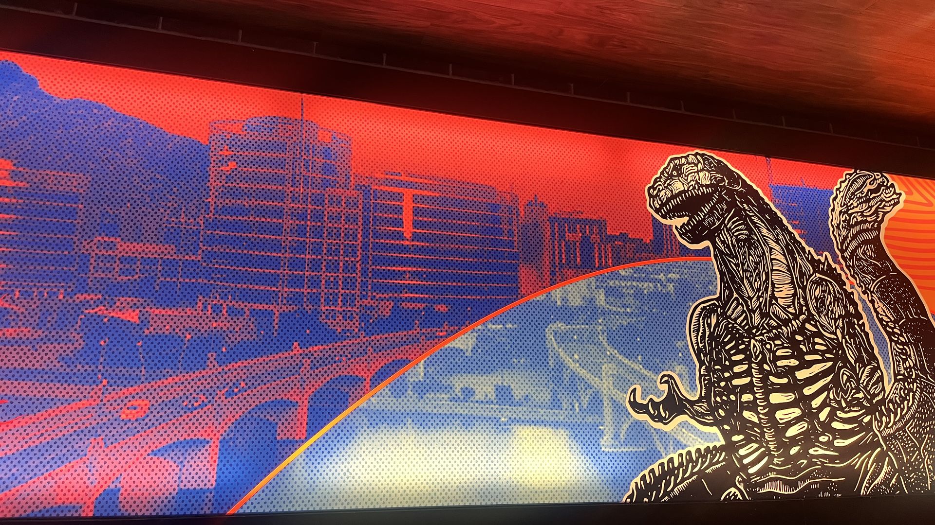 Artwork with a red and blue cityscape background and detailed black and white Godzilla-like monster illustration on the right, beneath a wood-textured ceiling vent.