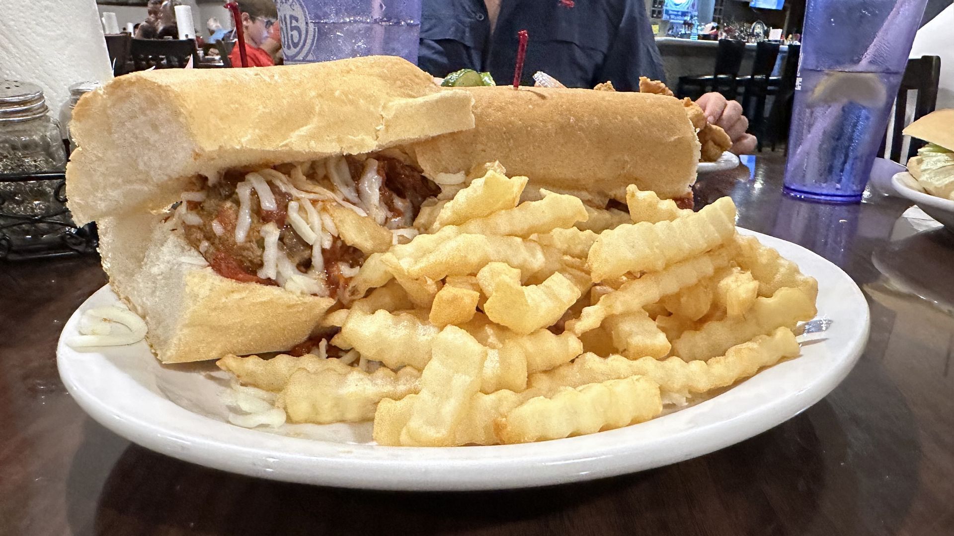 Photo shows a meatball poboy with French fries on a plate.