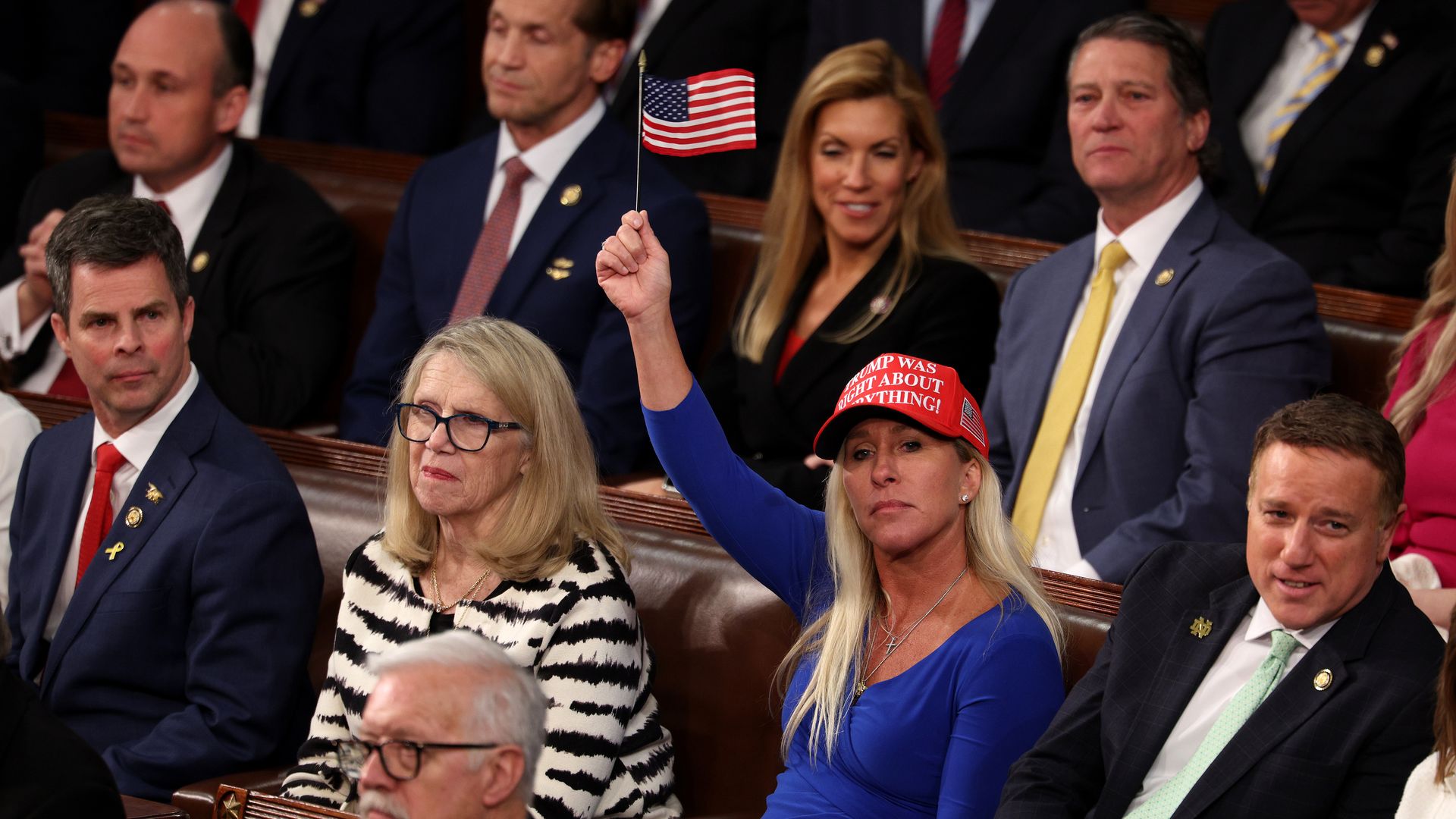 Rep. MTG wearing a MAGA hat and holding up an American flag in the House chamber 