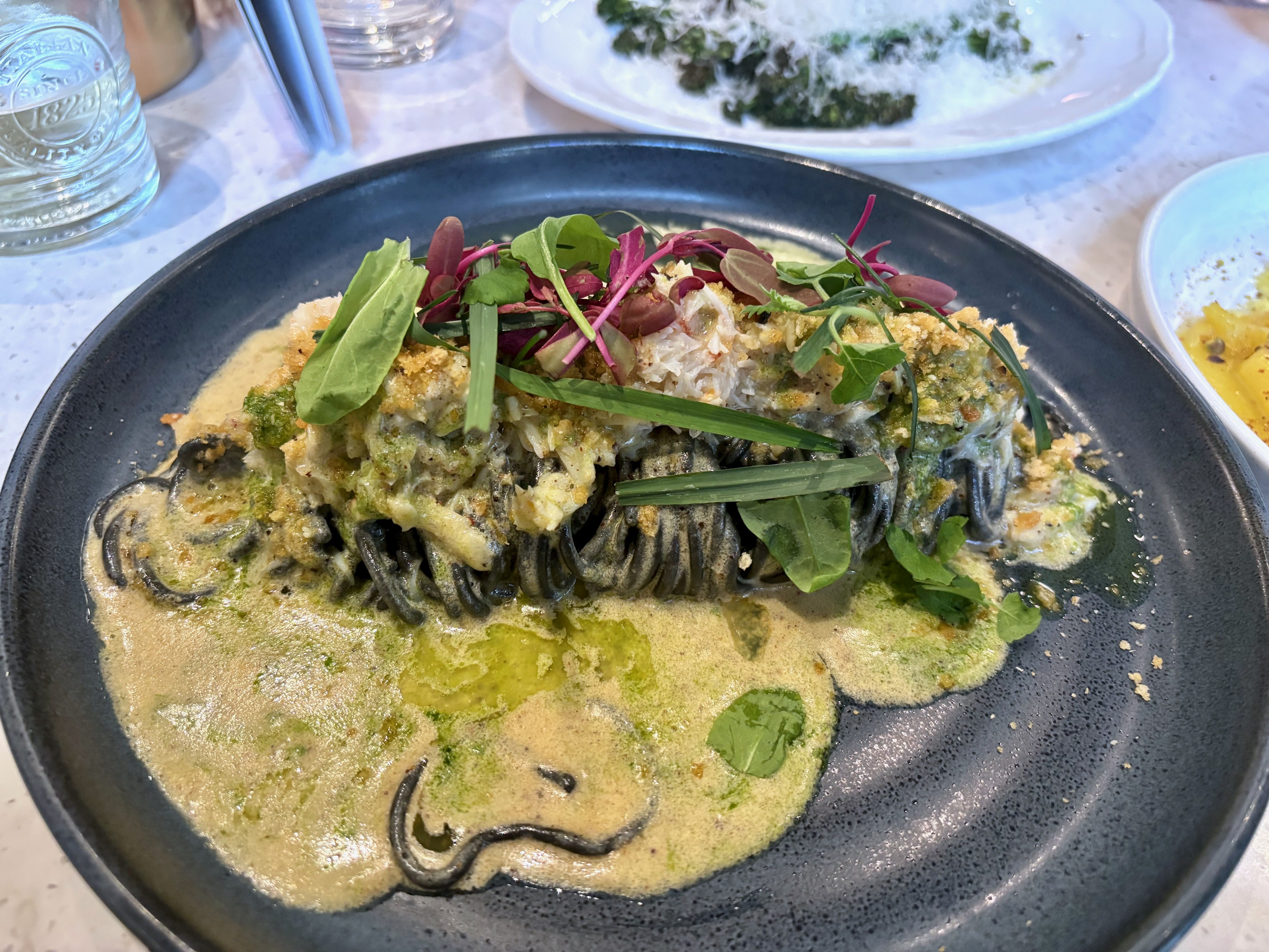 The crab pasta, with black spaghetti and a green and yellow sauce, topped with greens