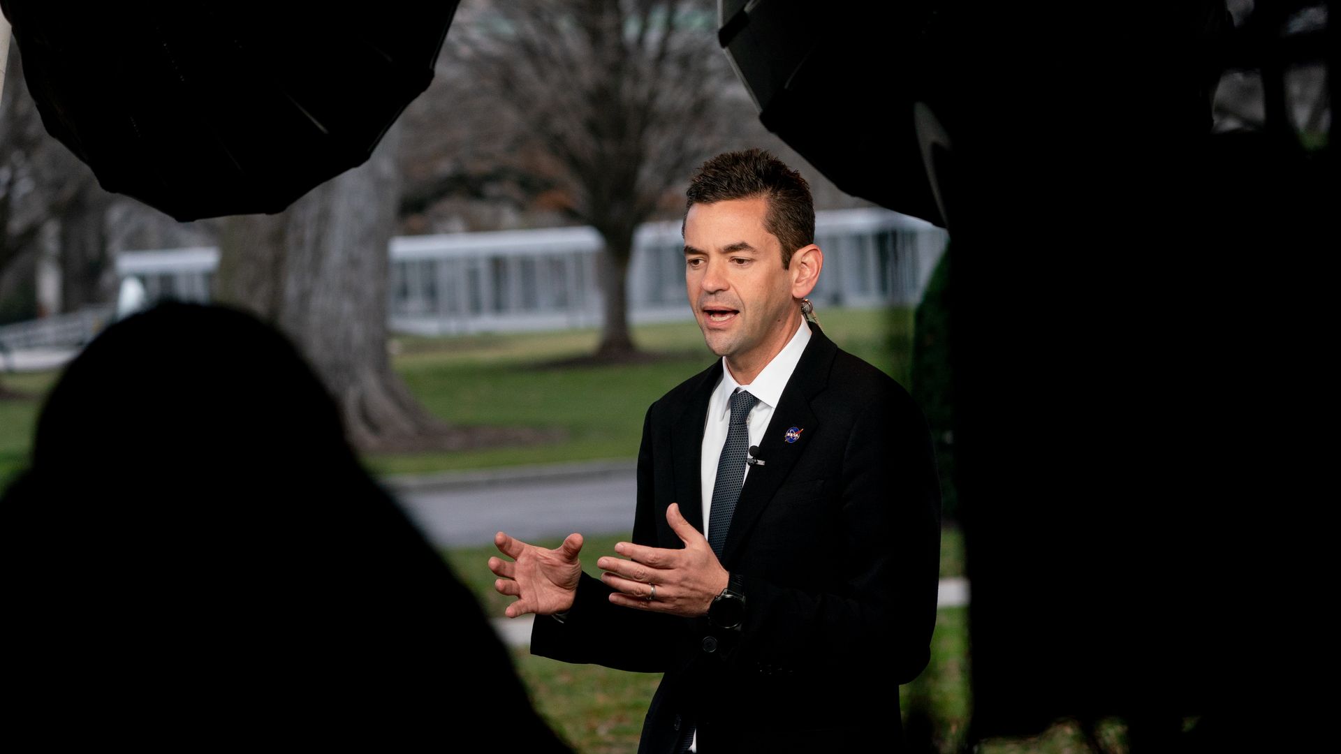 A man in a dark suit is show speaking to reporters.