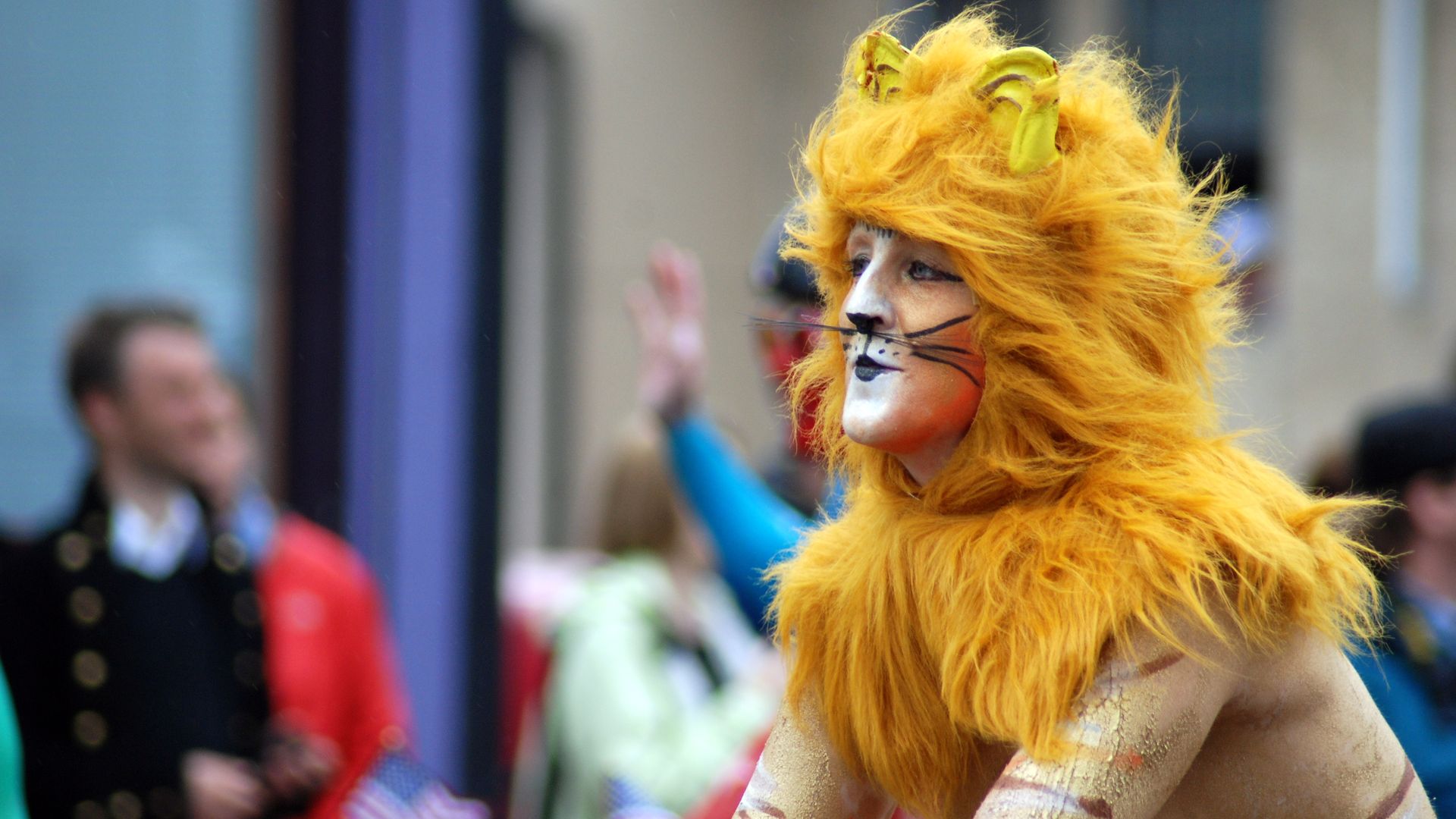 A main with his face painted like a lion with an orange mane rides a bike.