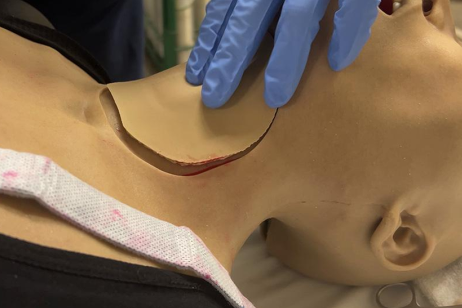 A mannequin with an incicision/neck wound and a gloved hand