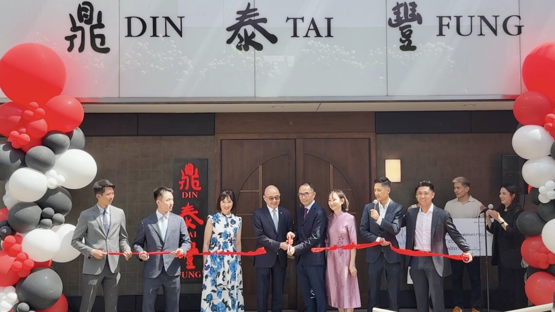 several people dressed in suits and dresses cutting a ribbon in front of a restaurant called Din Tai Fung