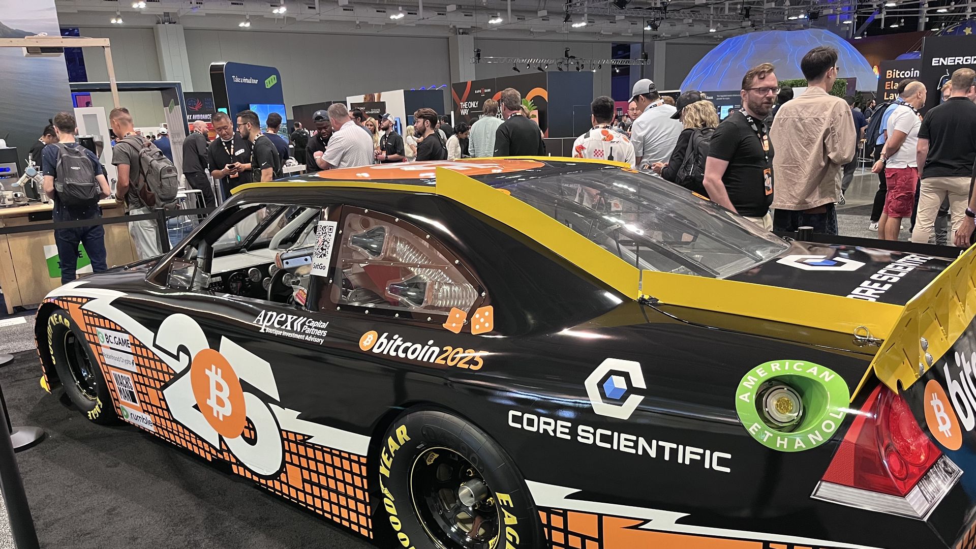 A racecar seen at a conference, with people milling around it. 