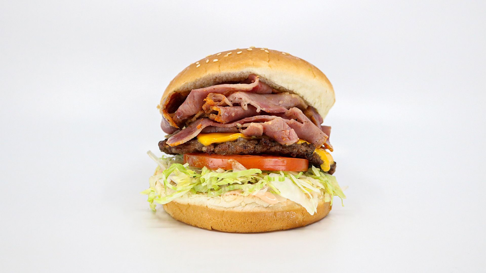 A burger with lettuce, tomato, cheese and pastrami.