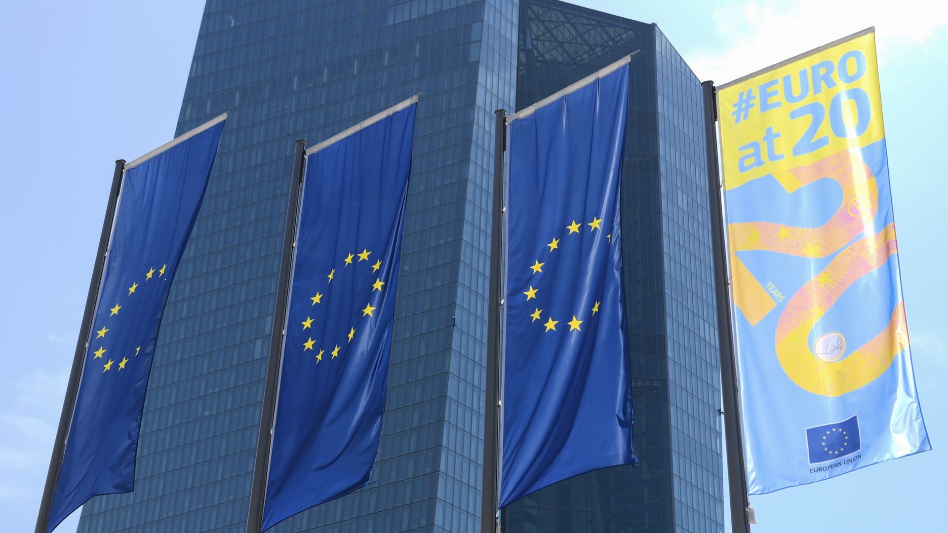 In this image, three EU flags hang from poles outside a skyscraper.
