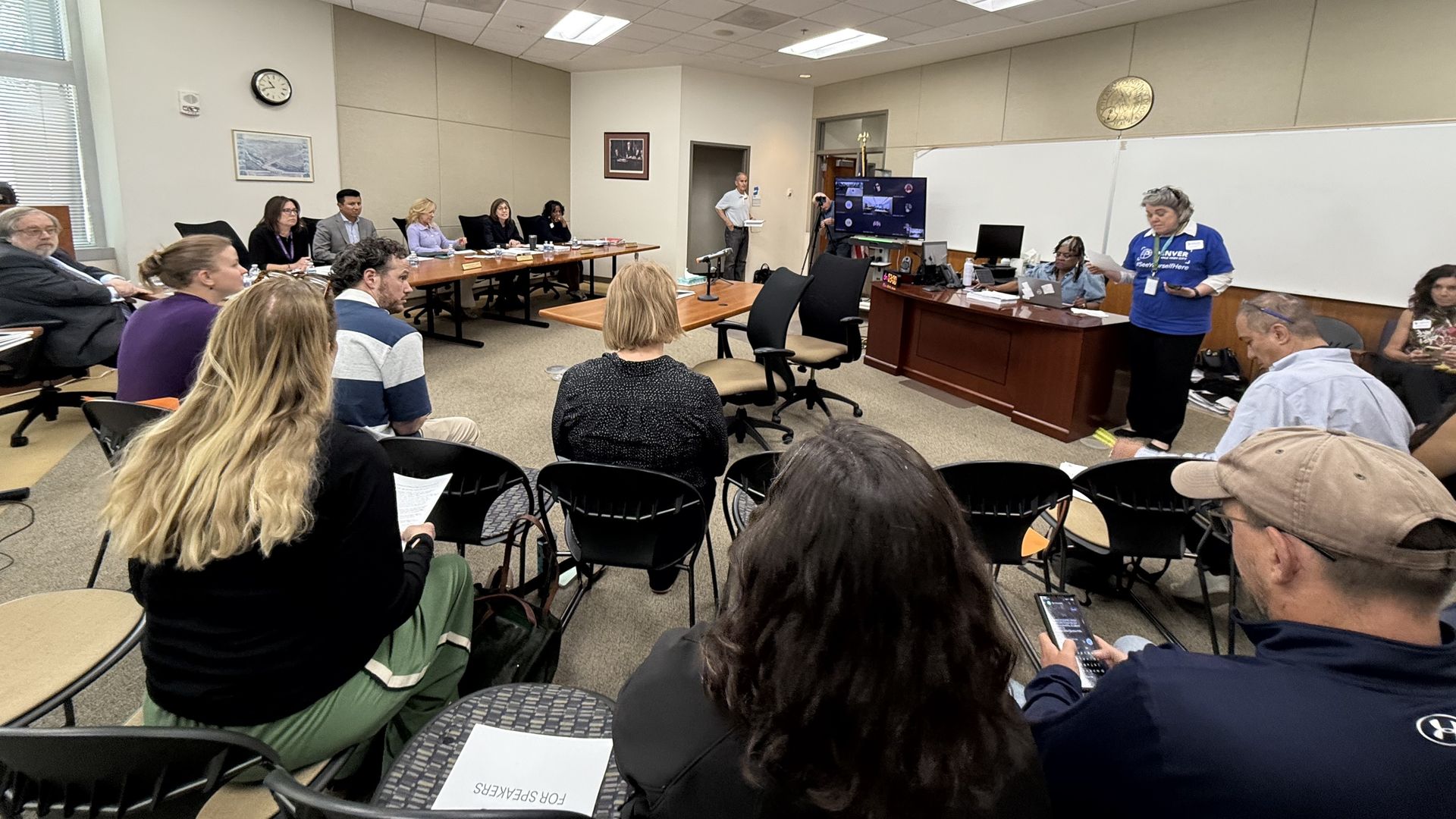 Numerous people stand inside a room. 
