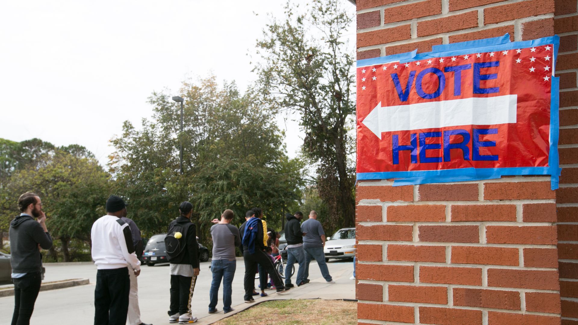Vote Here sign in all caps in red, white, and blue points to a line of voters in Georgia.