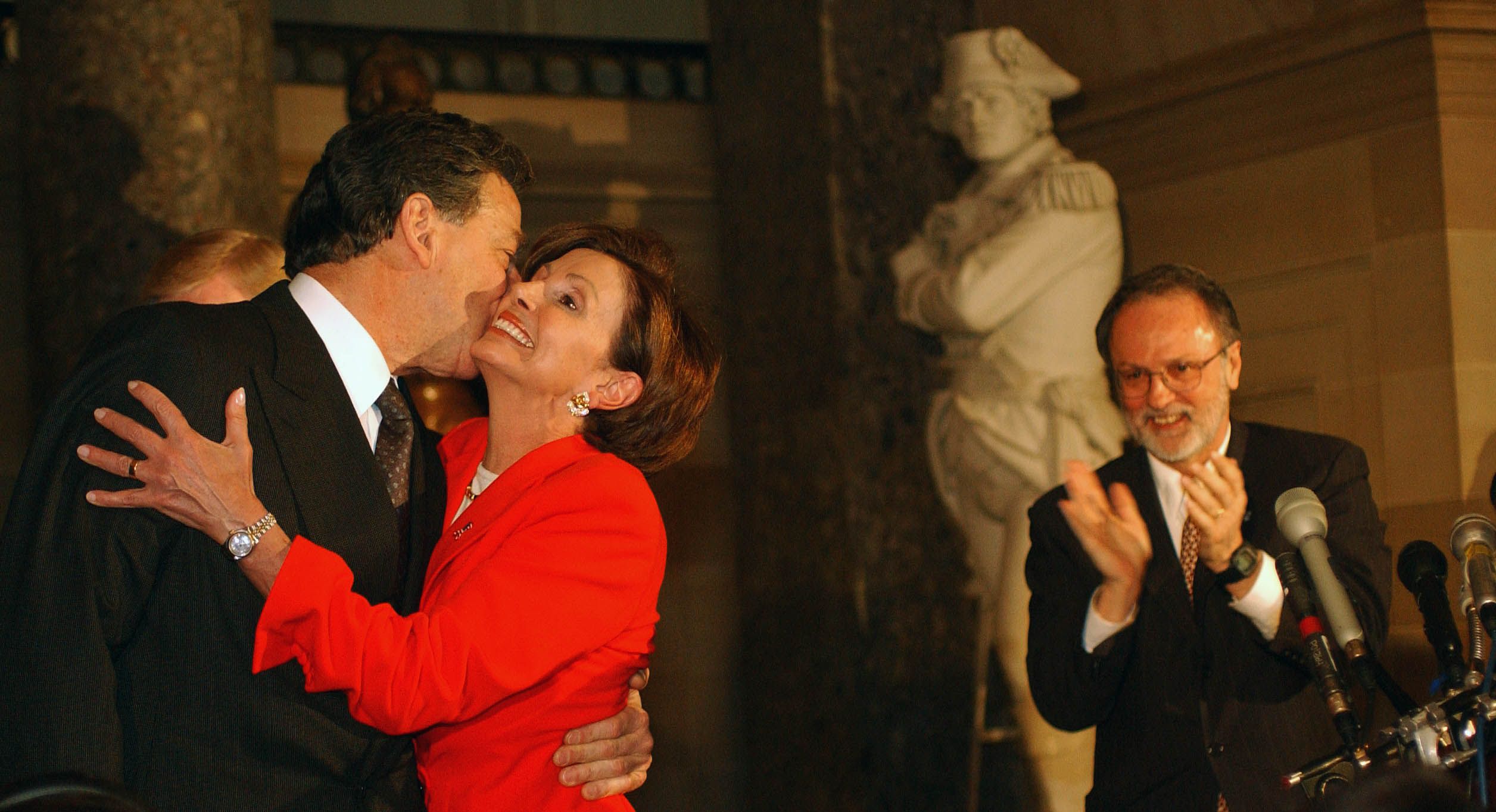 Nancy Pelosi embraces her husband, Paul, after being sworn in as House minority whip, with David Bonior watching nearby and clapping in Statuary Hall.