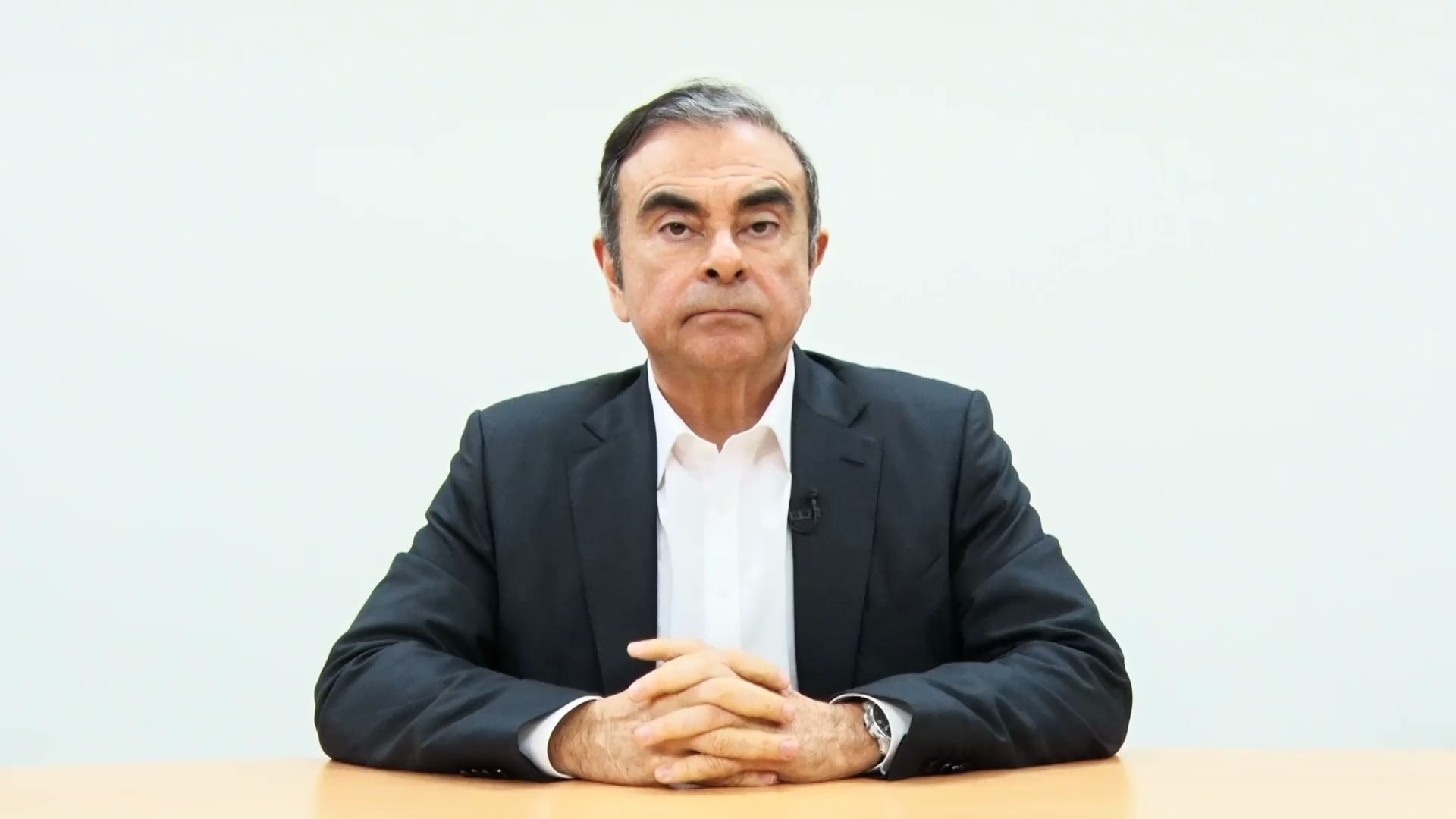Carlos Ghosn sitting at a table with his hands crossed.
