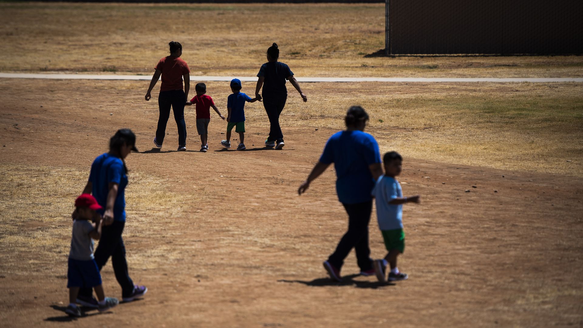 Children walk with women in a large dirt field