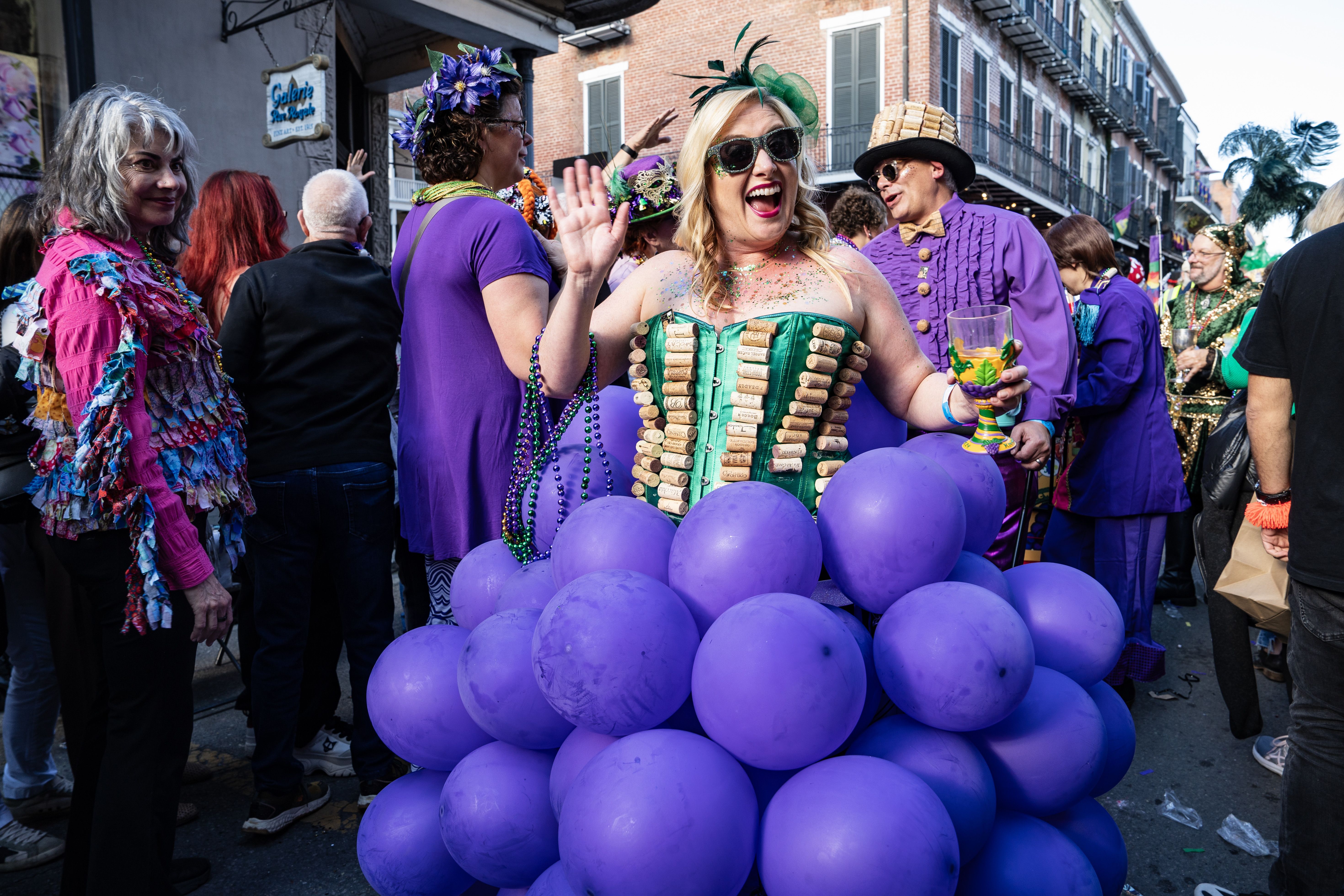 A woman dressed like grapes waves at the camera.