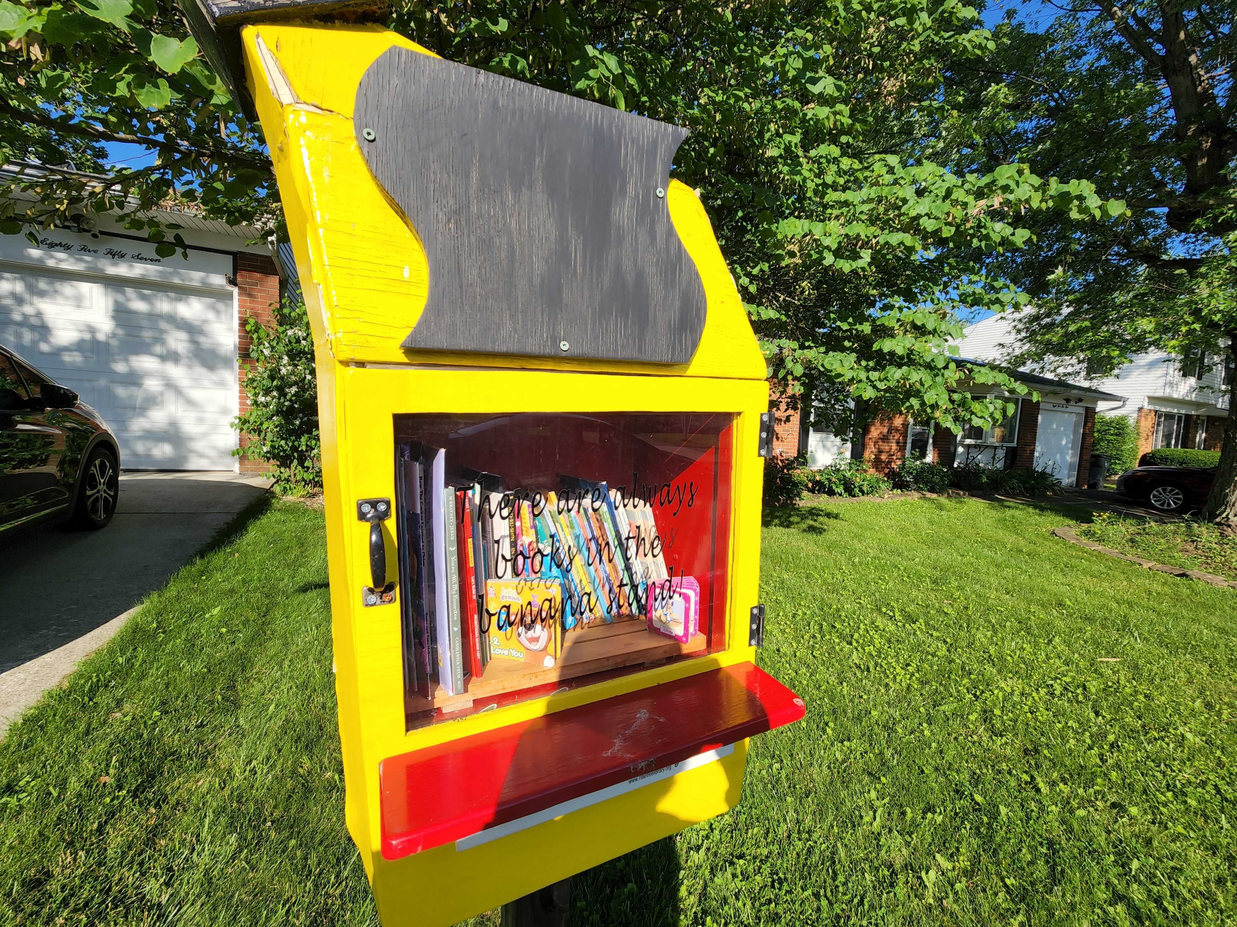 A yellow "Little Free Library" in a front yard.