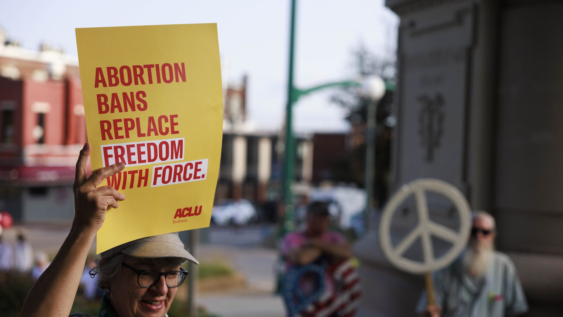 Picture of a person holding a yellow sign that says "abortion bans replace freedom with force"