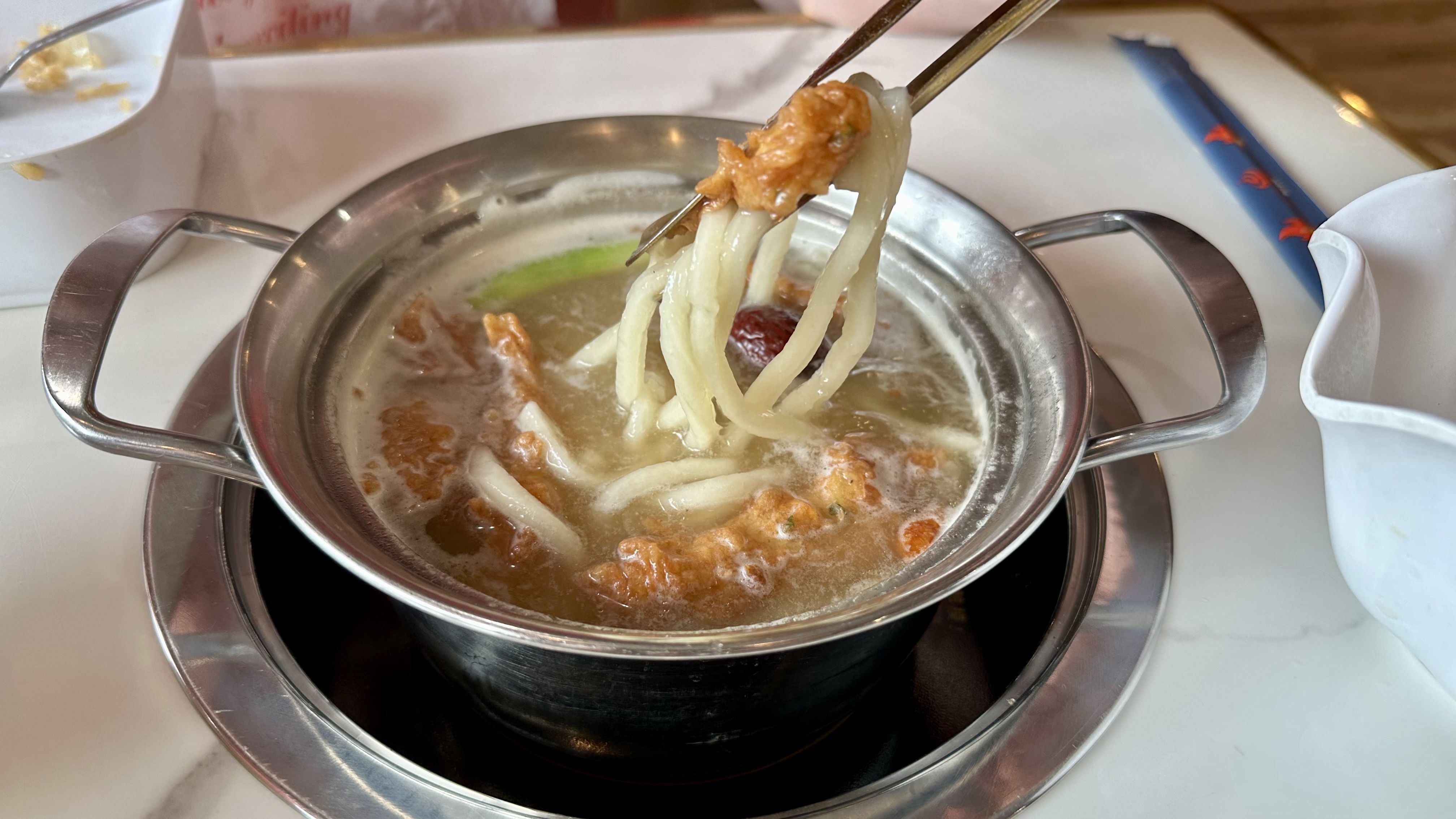Photo shows a pot of noodles and hot broth.