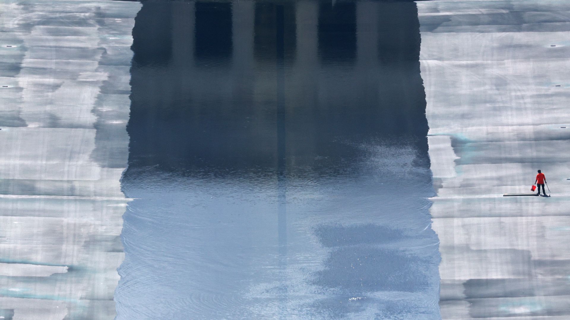 A lone worker, wearing red and carrying a bucket, tends the partially filled Lincoln Memorial Reflecting Pool.
