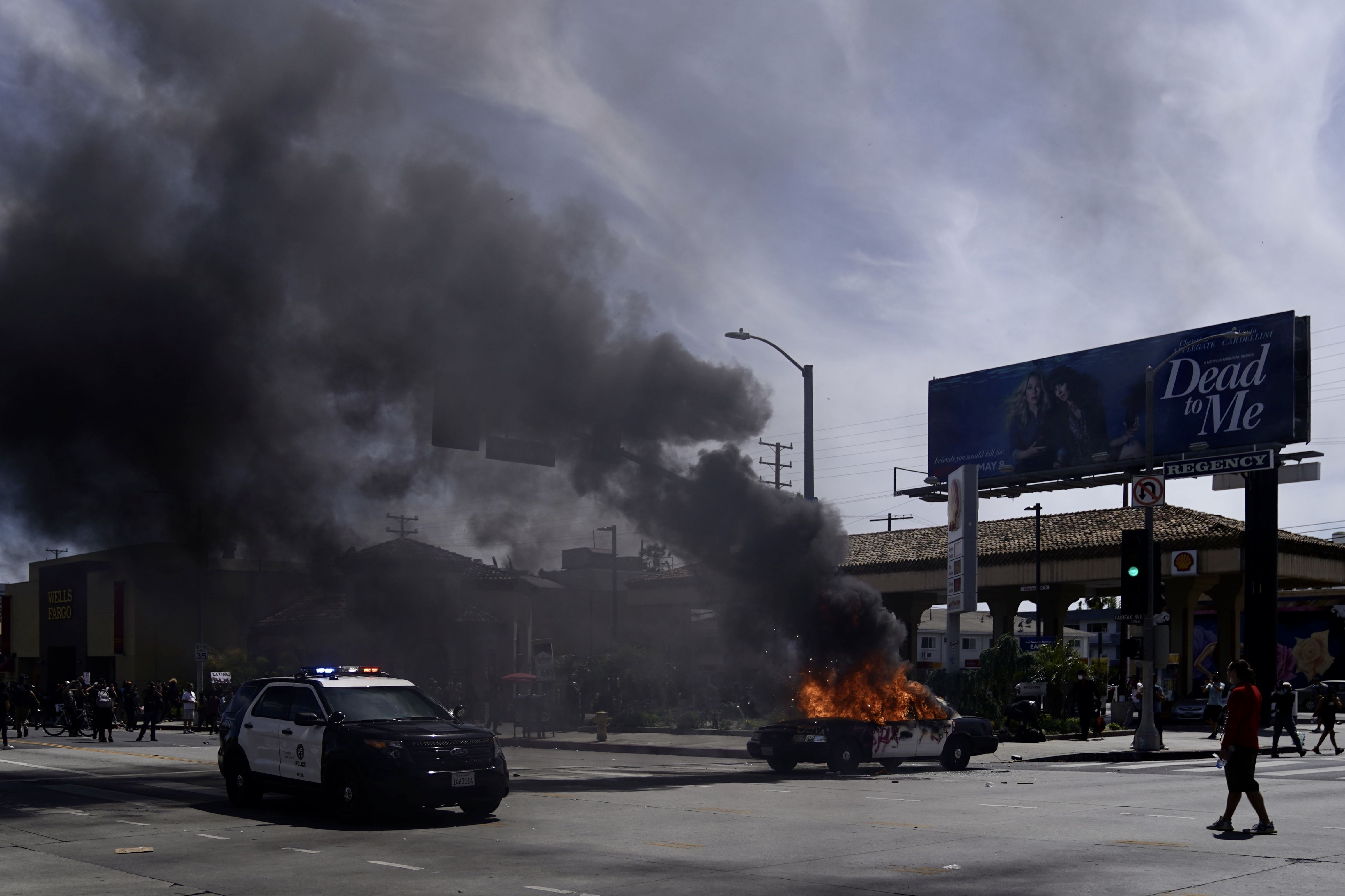 Groups of protesters gather in Los Angeles as police cars burn in a fire