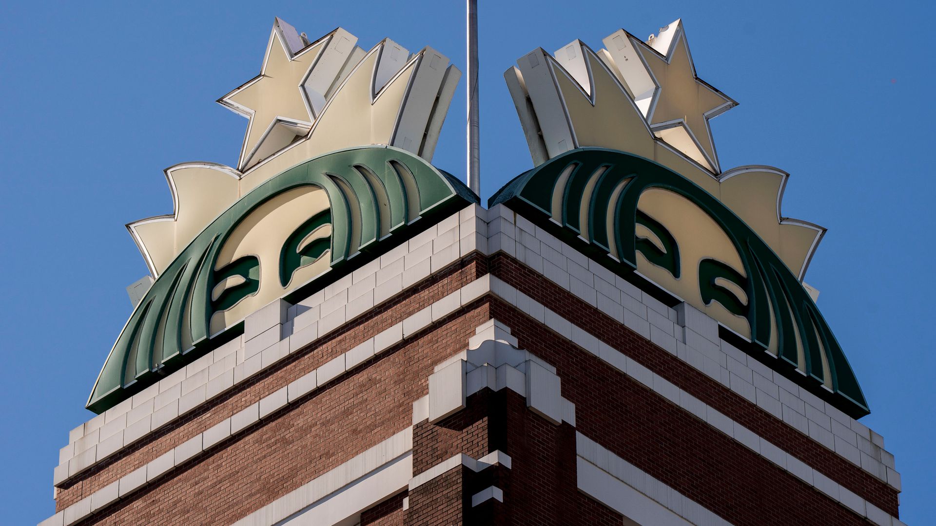 Two Starbucks mermaid logos seen against a blue sky atop the company's brick headquarters in Seattle. 