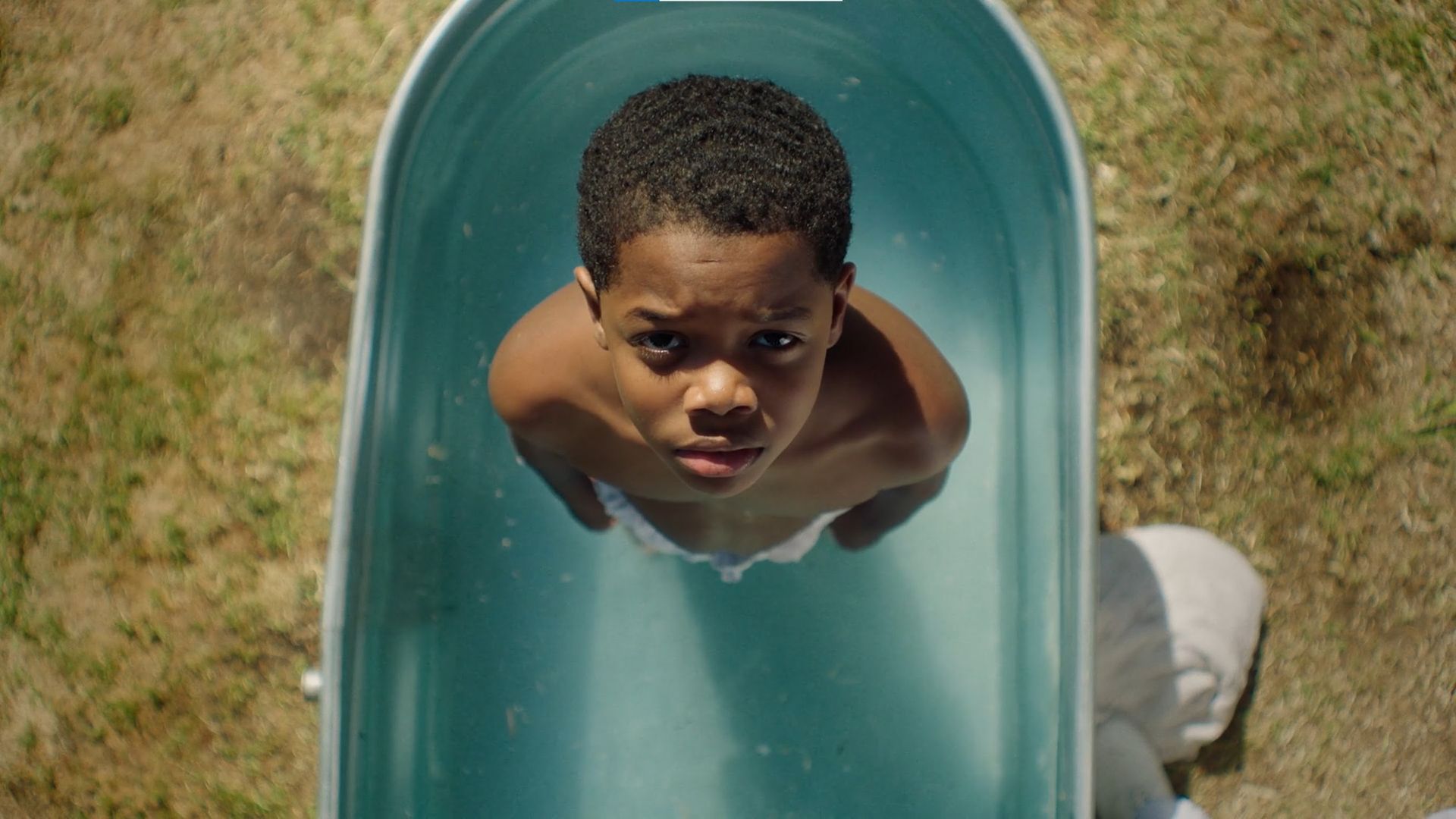 A young boy standing in a wash basin looks up toward the sky and into the camera