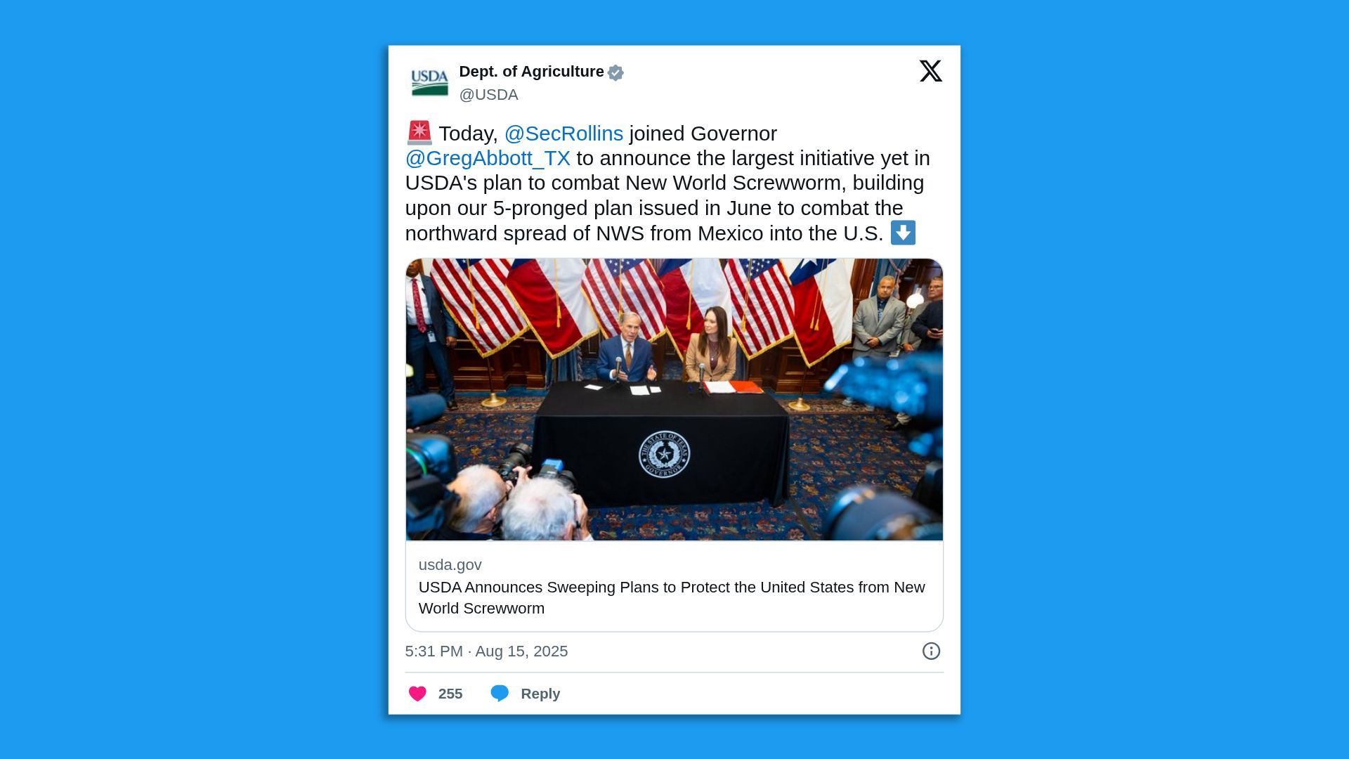 Photo of a press conference with two officials at a table covered with a Texas state seal cloth, surrounded by Texas and US flags, as photographers capture the event.